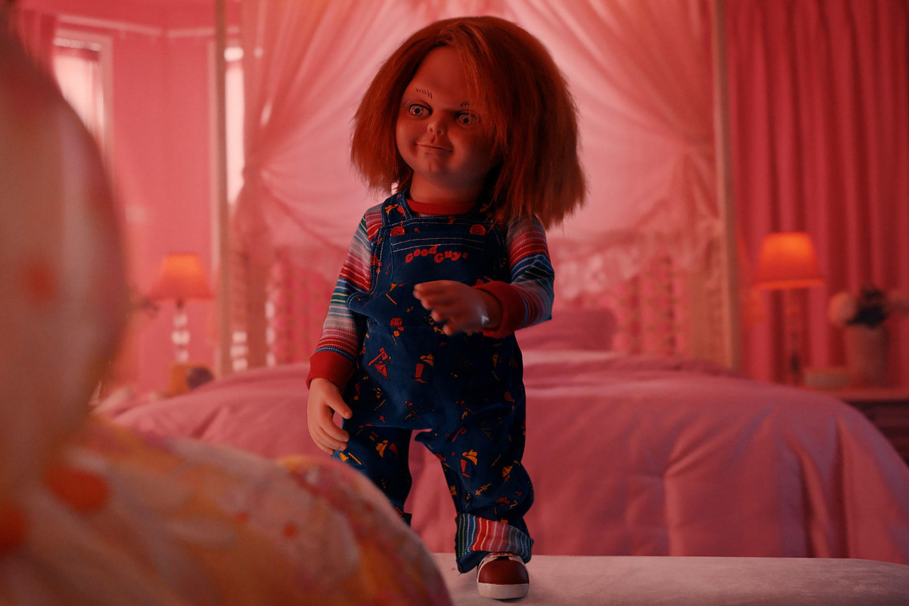 Chucky-Puppe in blauer Latzhose steht im rosa Zimmer.