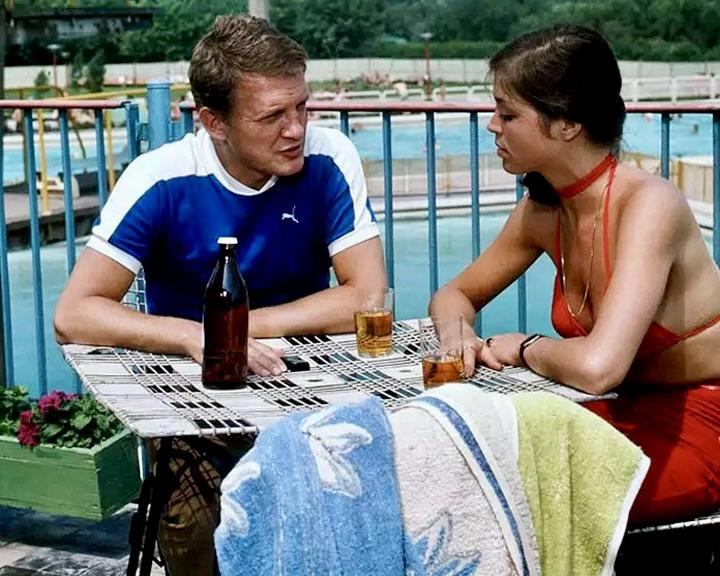 Mann und Frau sitzen an einem Tisch mit Getränken und einer Flasche Bier am Pool.