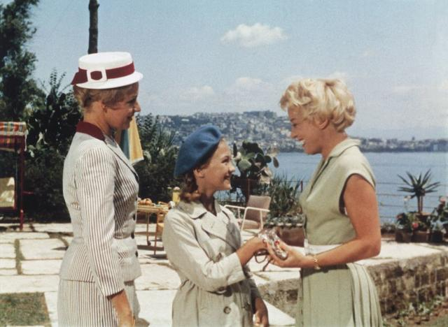 Drei Frauen stehen auf einer Terrasse mit Blick auf das Meer und eine Stadt.