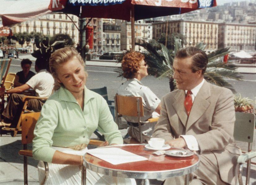 Ein Paar sitzt an einem Tisch im Freien in einem Café. Gebäude im Hintergrund.
