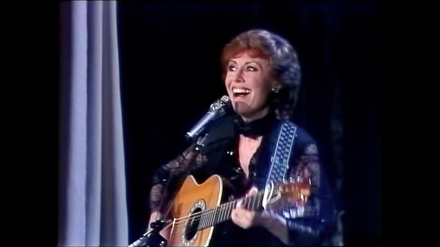Eine Frau mit roten Haaren spielt Gitarre und singt in ein Mikrofon.