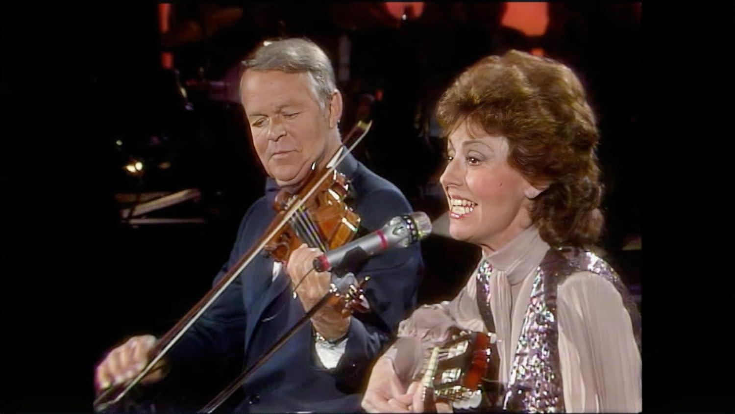 Ein Mann spielt Geige, eine Frau singt und spielt Gitarre auf einer Bühne.