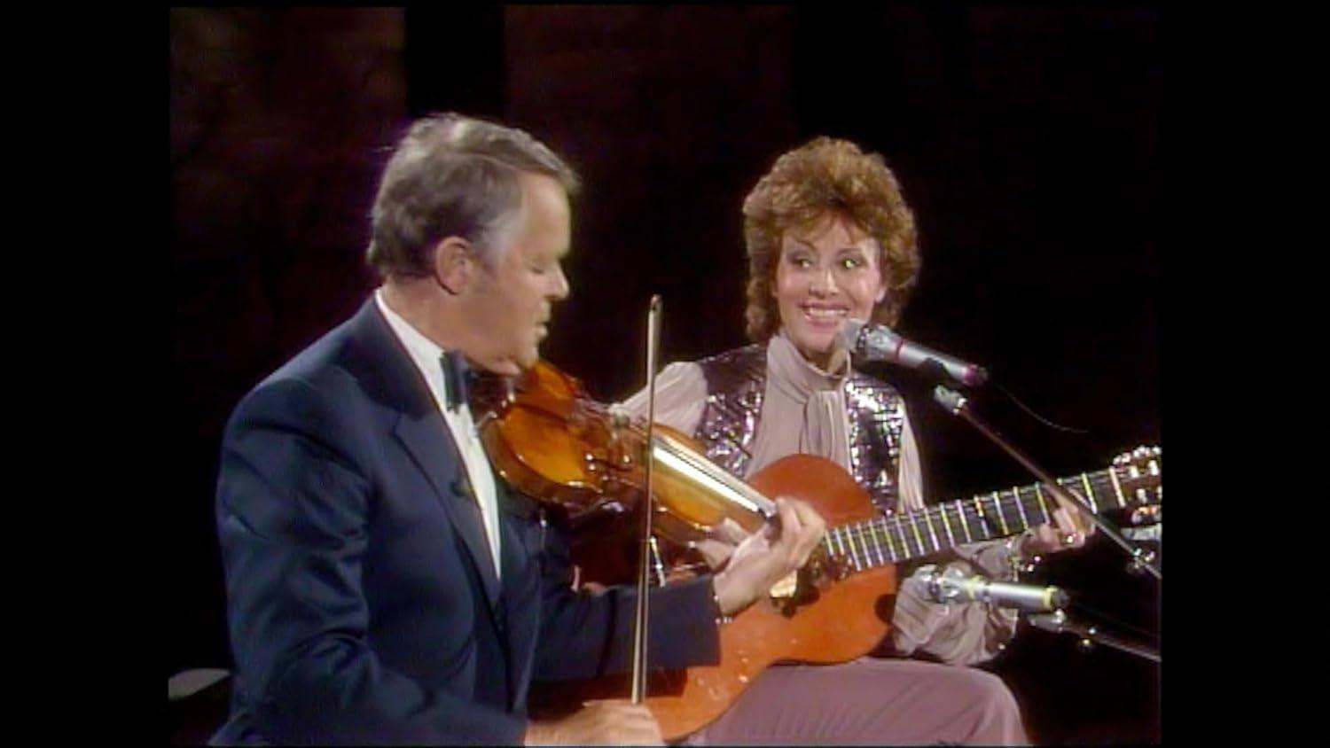Ein Mann spielt Violine, eine Frau spielt Gitarre und singt in ein Mikrofon.