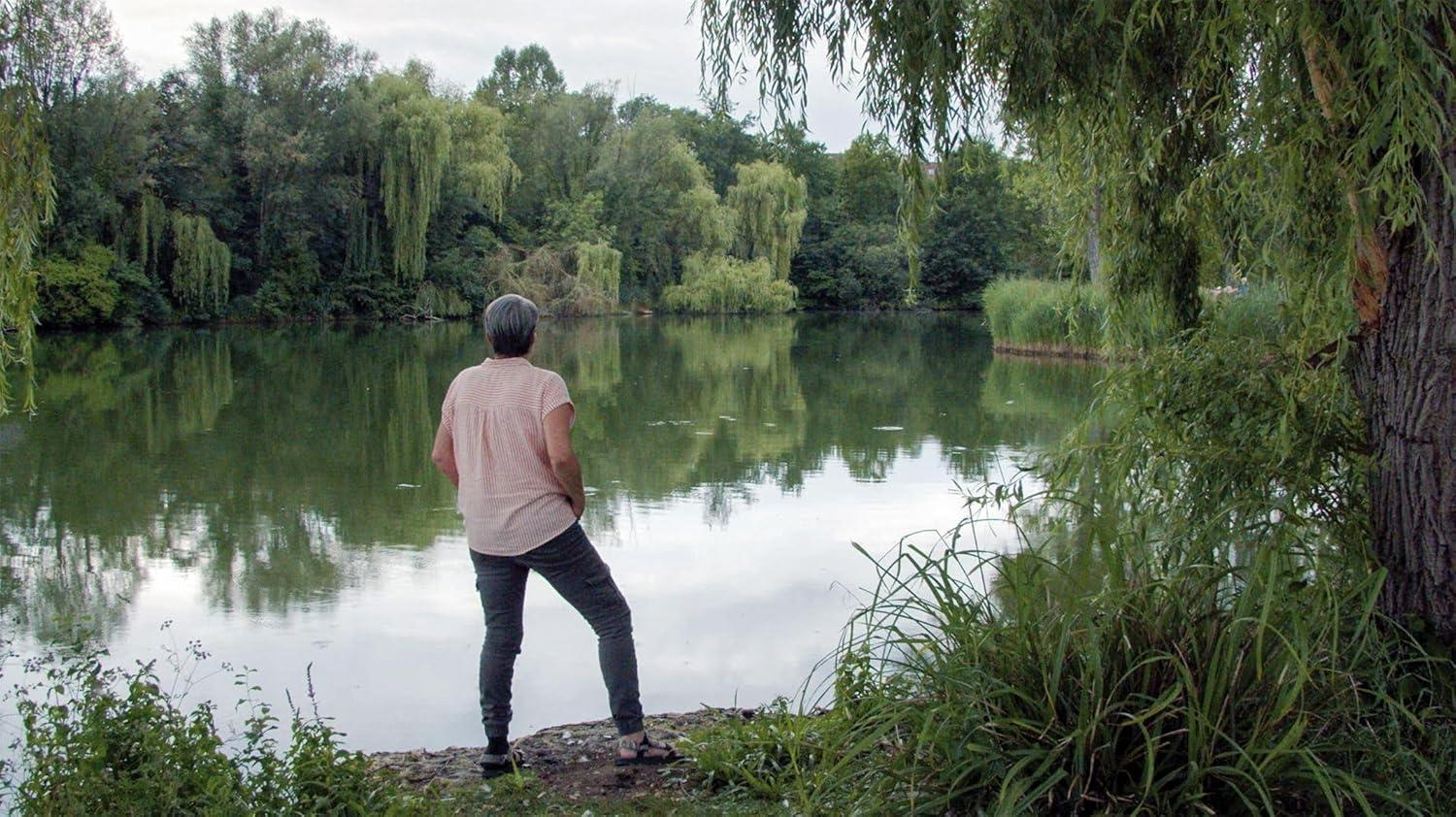 Eine Frau steht am Ufer eines ruhigen Sees mit üppiger Vegetation.