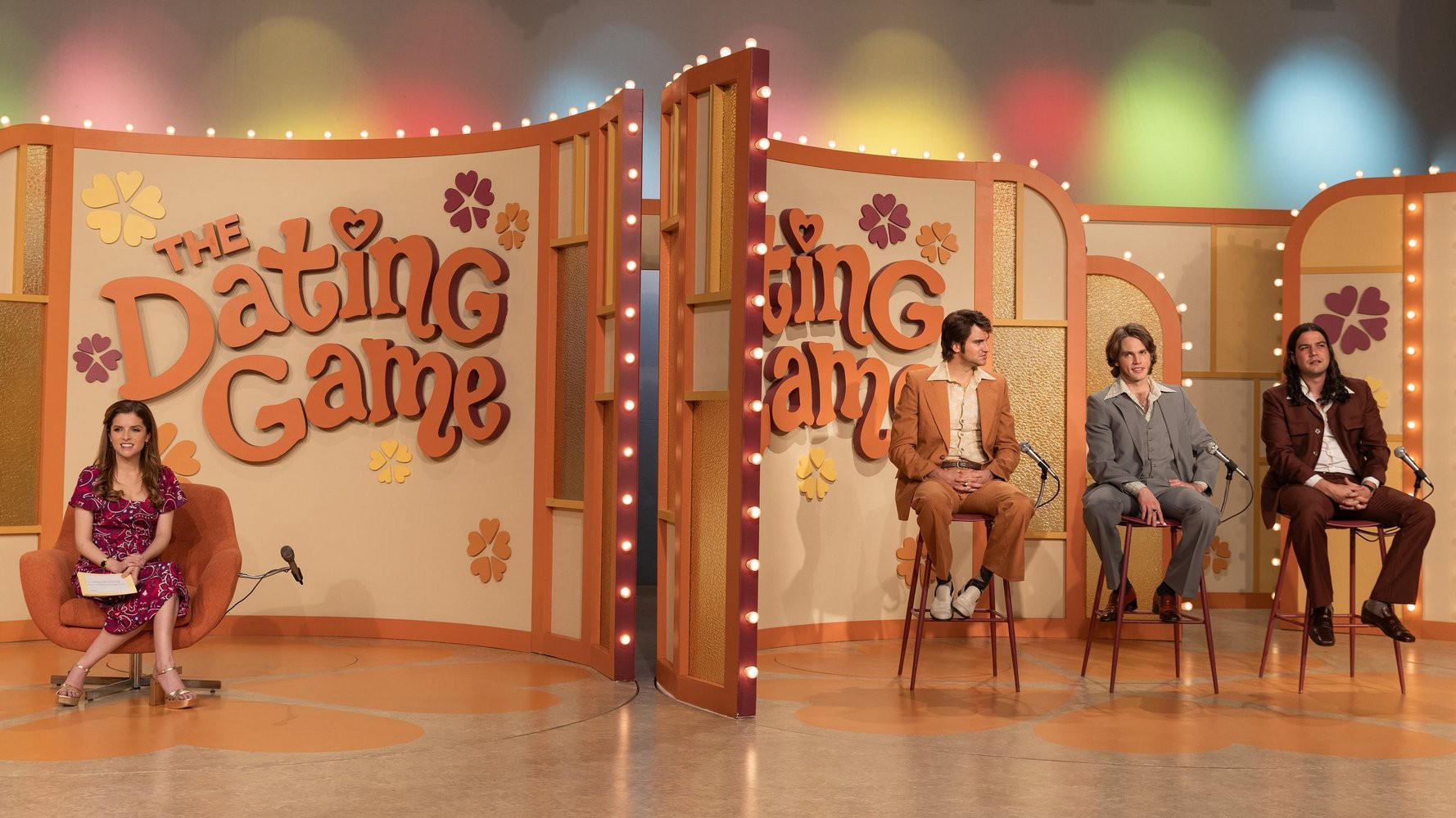 Vier Personen sitzen auf einem Fernsehset von "The Dating Game" mit Blumenmotiven.