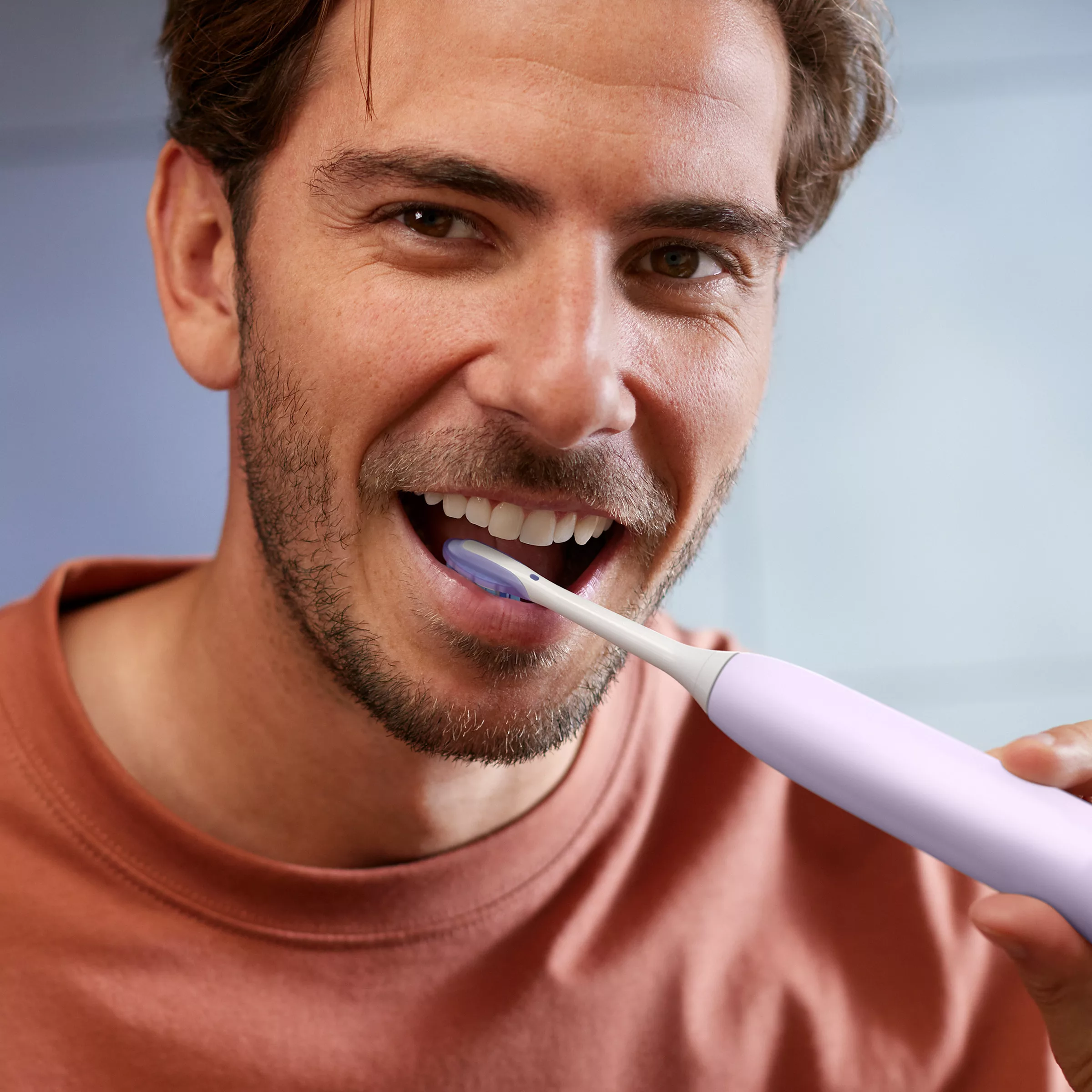 Mężczyzna z brodą myje zęby szczoteczką elektryczną.