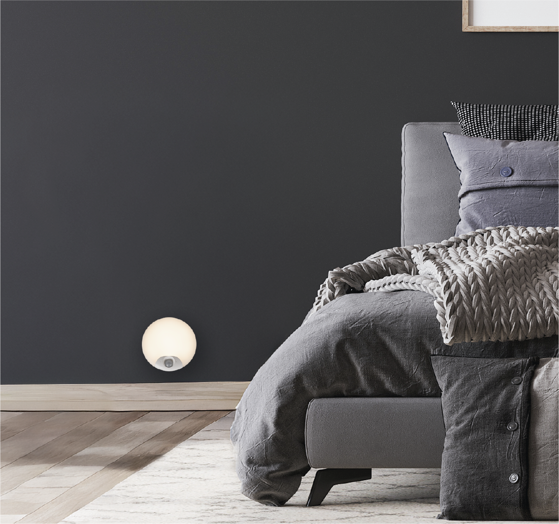 Een rond nachtlampje gloeit op een donkere muur naast een bed.
