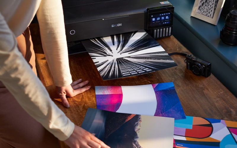 Drukarka drukuje czarno-białe zdjęcie. W pobliżu leżą zdjęcia.