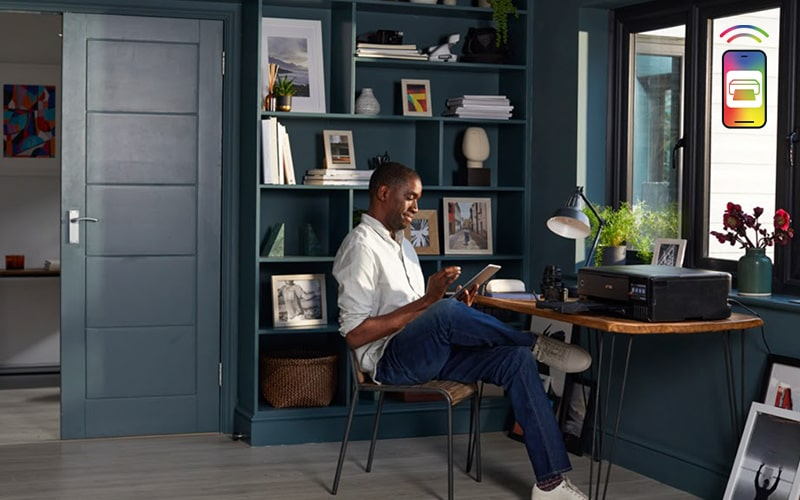 Mężczyzna siedzi przy biurku i używa tabletu. Drukarka na biurku.