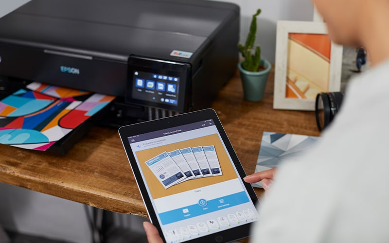 Drukarka drukuje kolorowy arkusz, obok osoba obsługuje tablet.