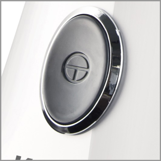 Owalny czarny przycisk z chromowaną krawędzią na białym urządzeniu.