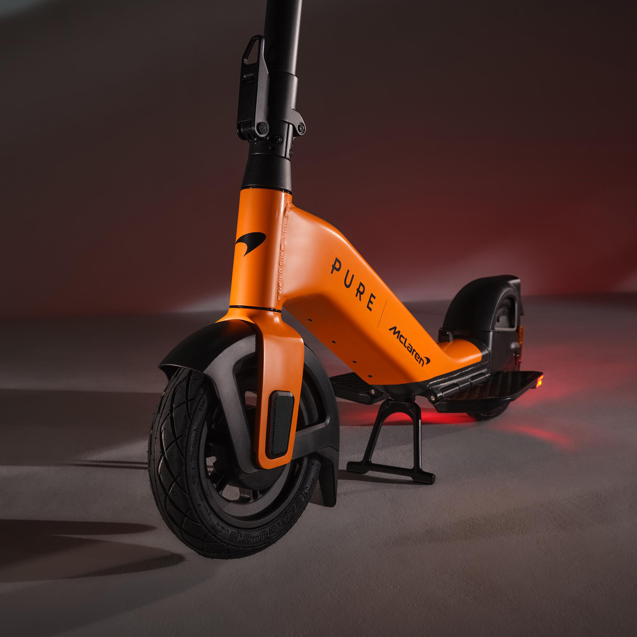 Orange E-Scooter mit McLaren-Logo, Details in Schwarz, auf dunklem Hintergrund.
