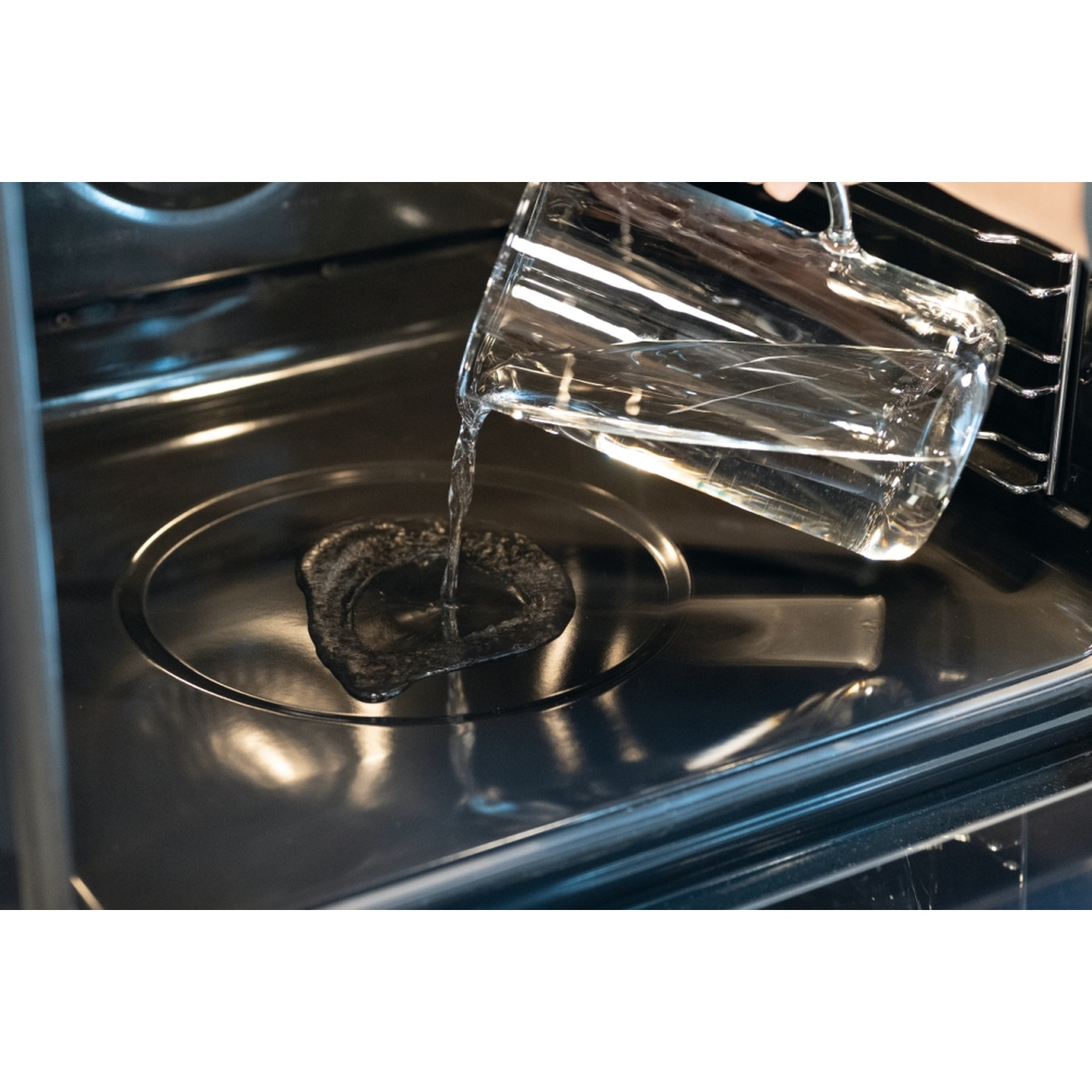 Acqua limpida versata da un bicchiere in un forno scuro.