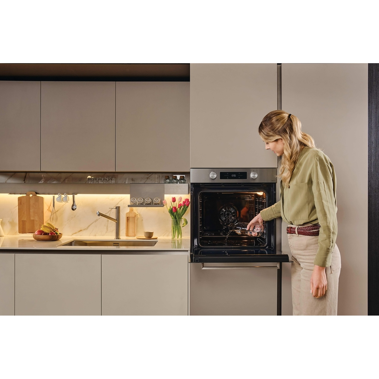 Una donna bionda mette un bicchiere in un forno aperto in una cucina moderna.
