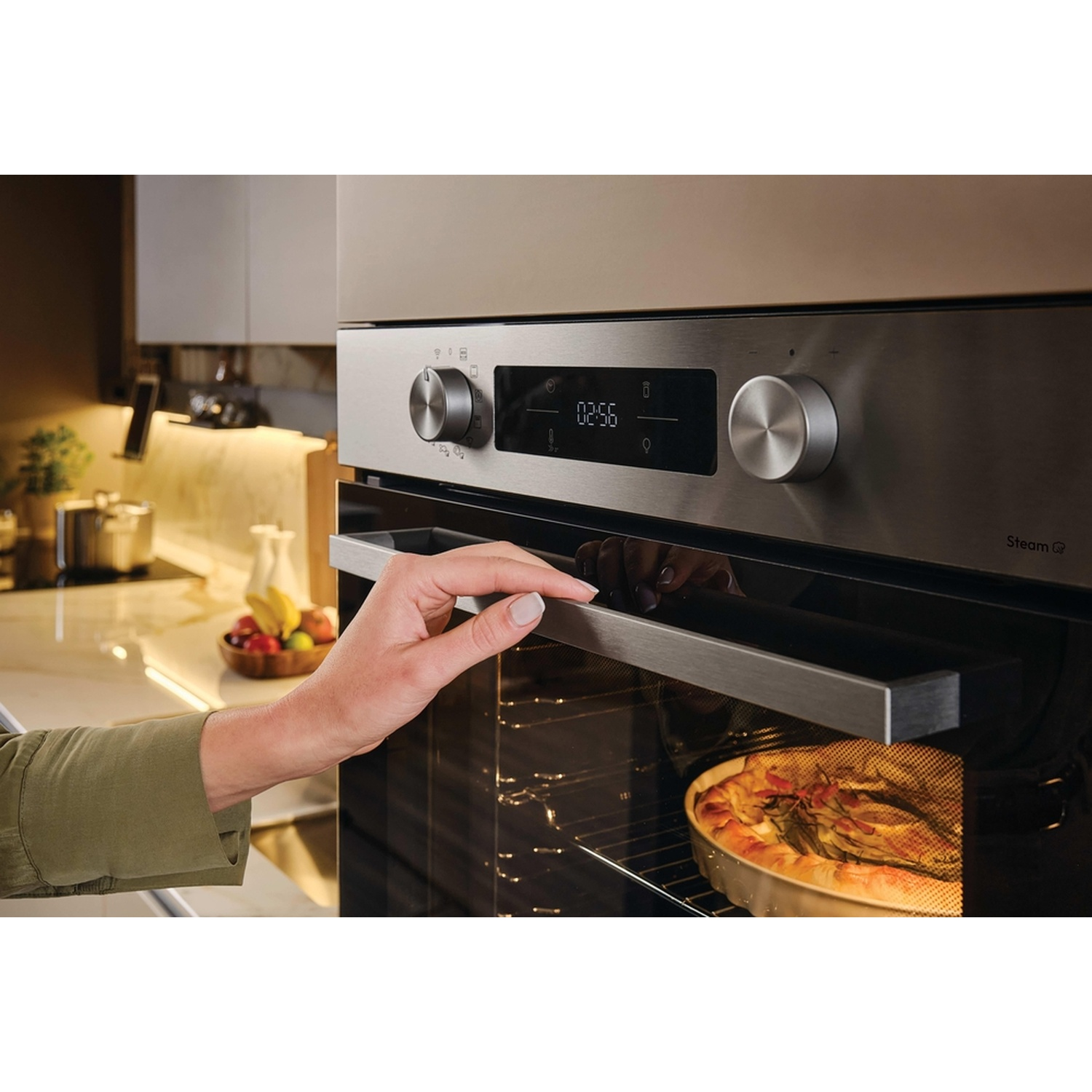 Una mano apre un forno moderno con una torta all'interno. Display digitale mostra 02:56.