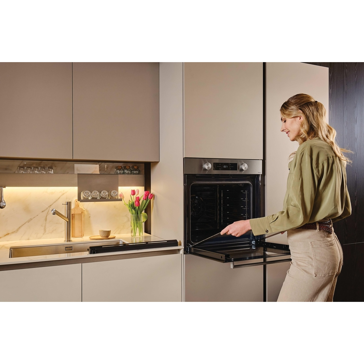 Una donna apre lo sportello di un moderno forno da cucina. Accanto c'è un lavello.