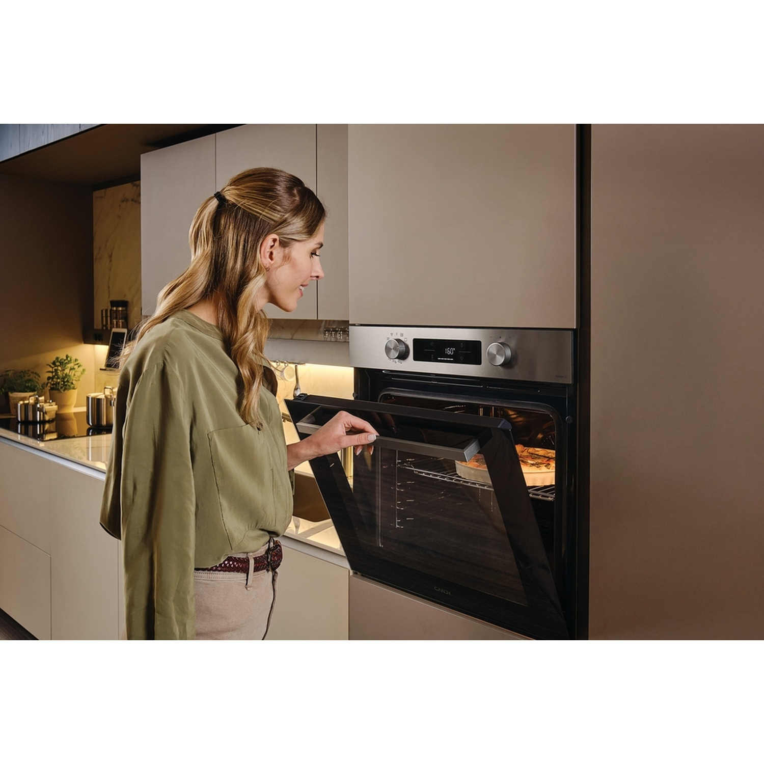 Donna apre un forno in una cucina moderna con un piatto di vetro all'interno.