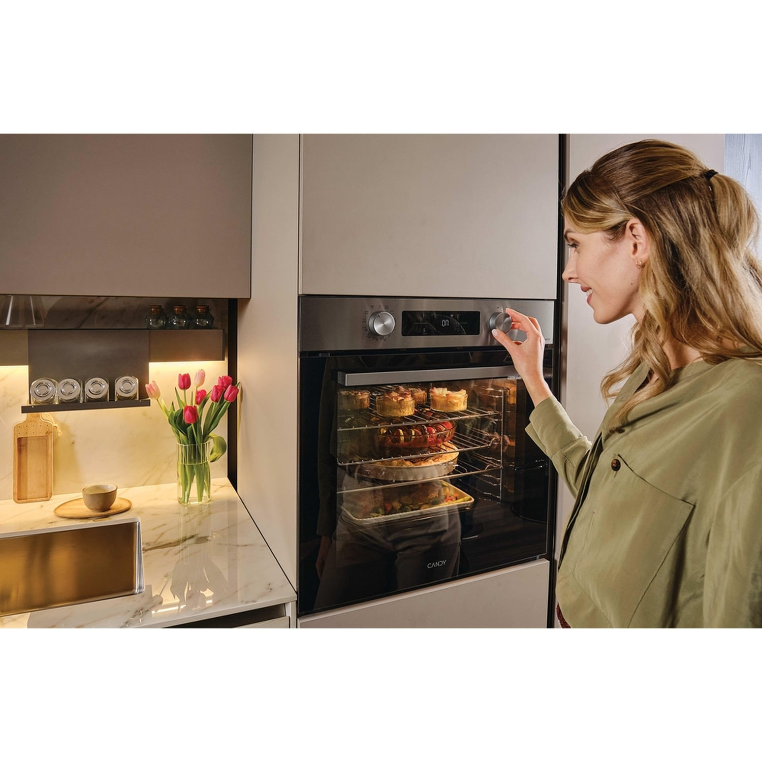 Una donna regola il forno dove torte e casseruole cuociono sui ripiani.