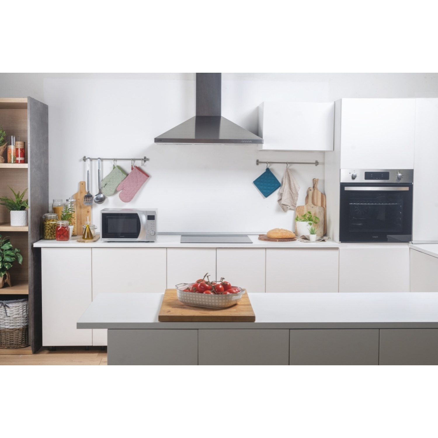 Cucina moderna con microonde, forno, piano cottura e pomodori su tagliere.
