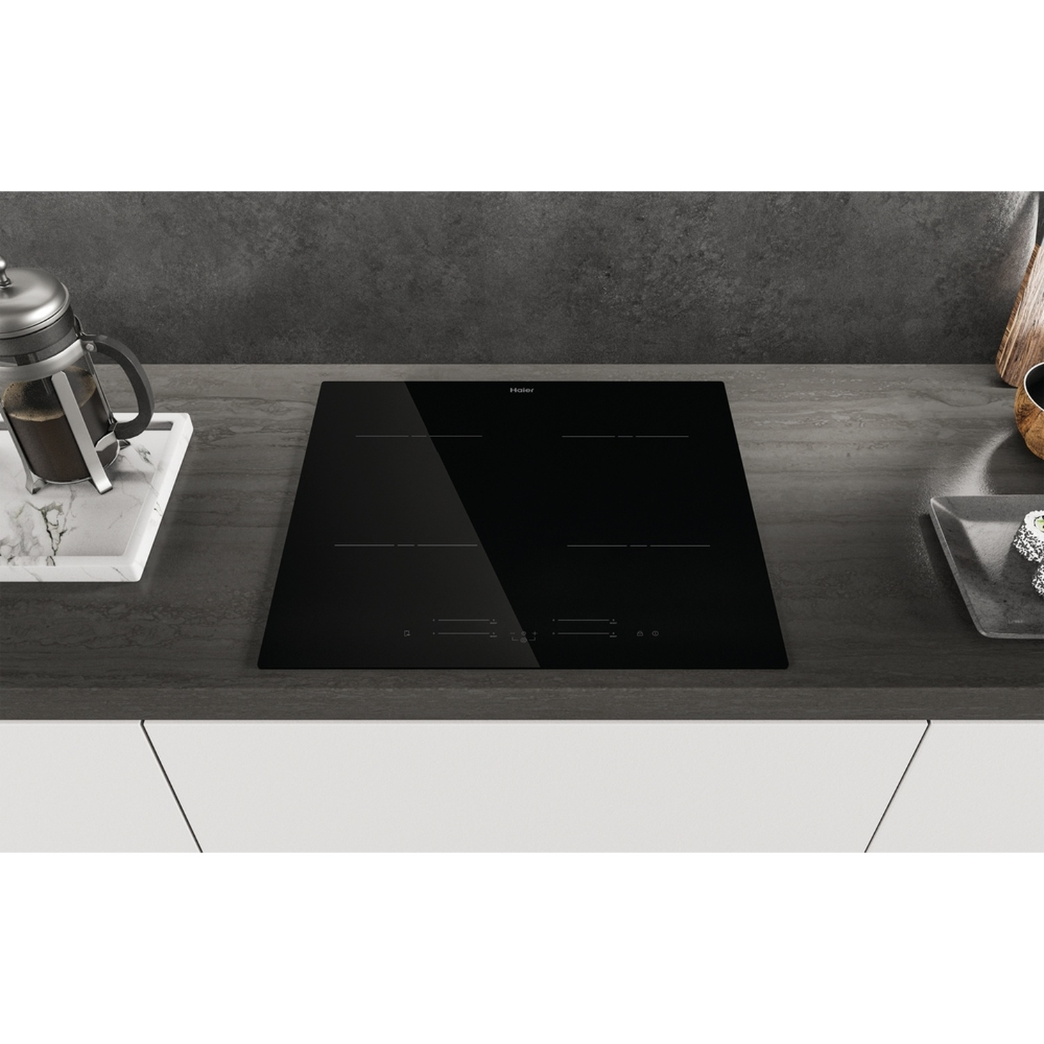 Un piano cottura a induzione nero con quattro zone di cottura, accanto a una caffettiera.
