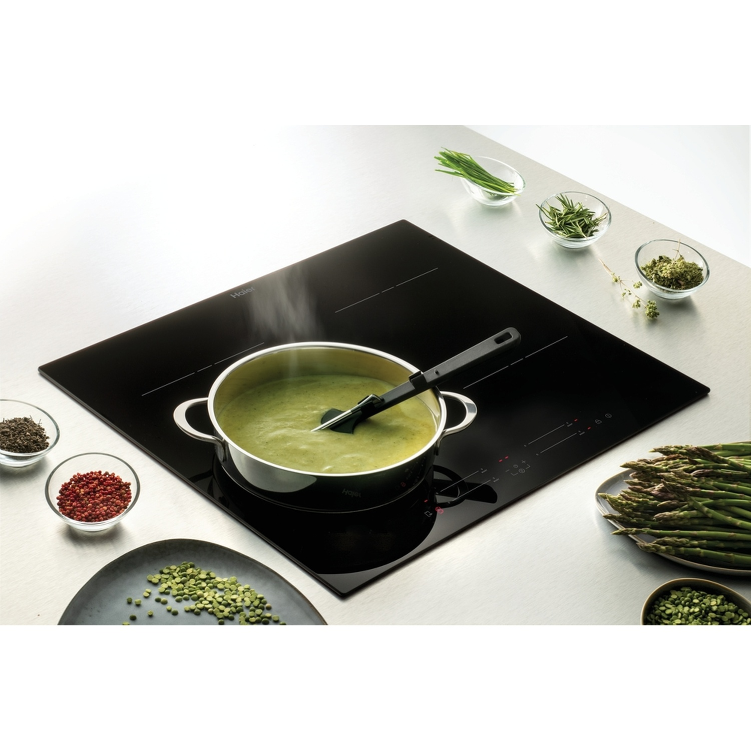 Zuppa verde sobbolle in una pentola su piano cottura a induzione, con asparagi ed erbe aromatiche.