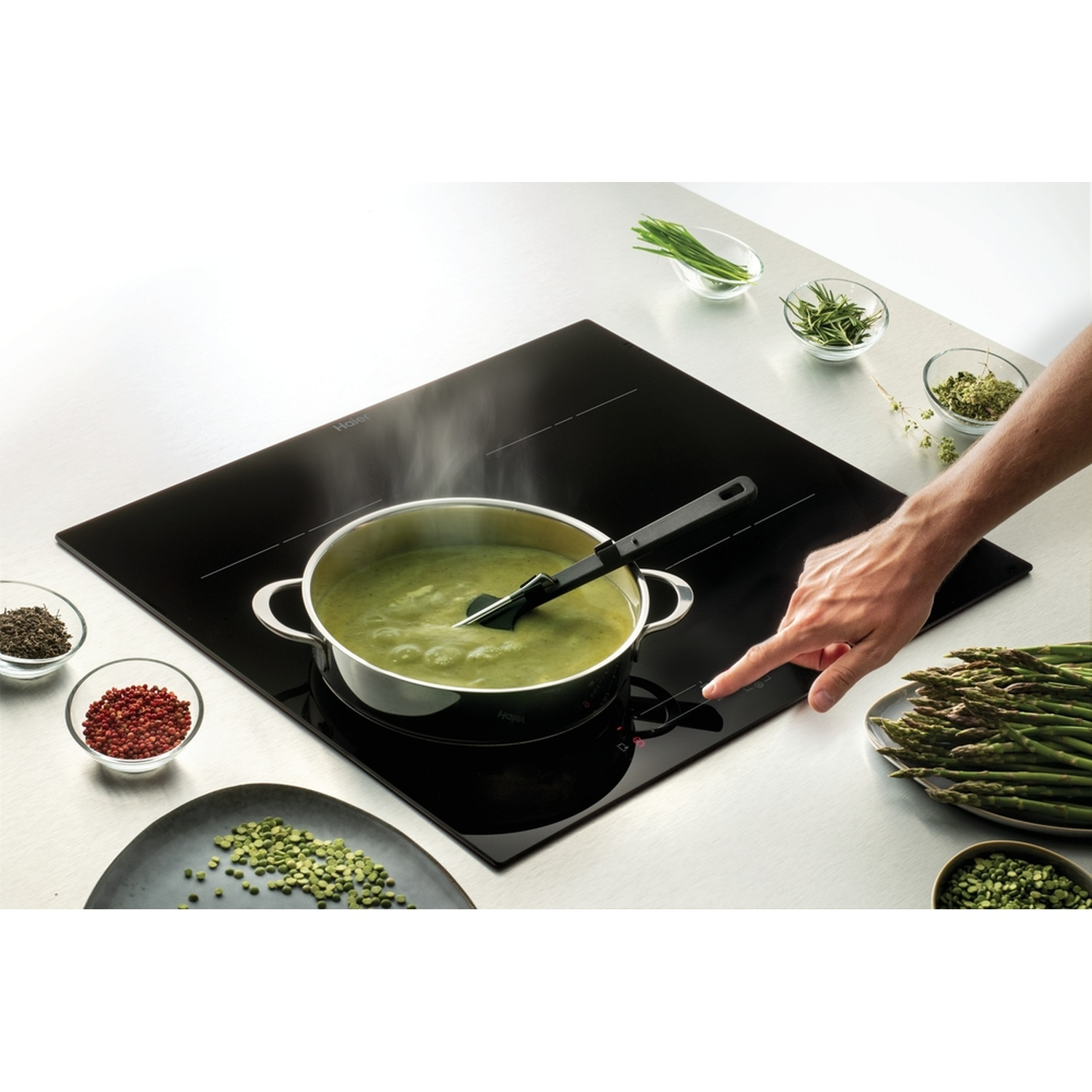 Zuppa verde sobbolle su piano cottura a induzione, con asparagi ed erbe.