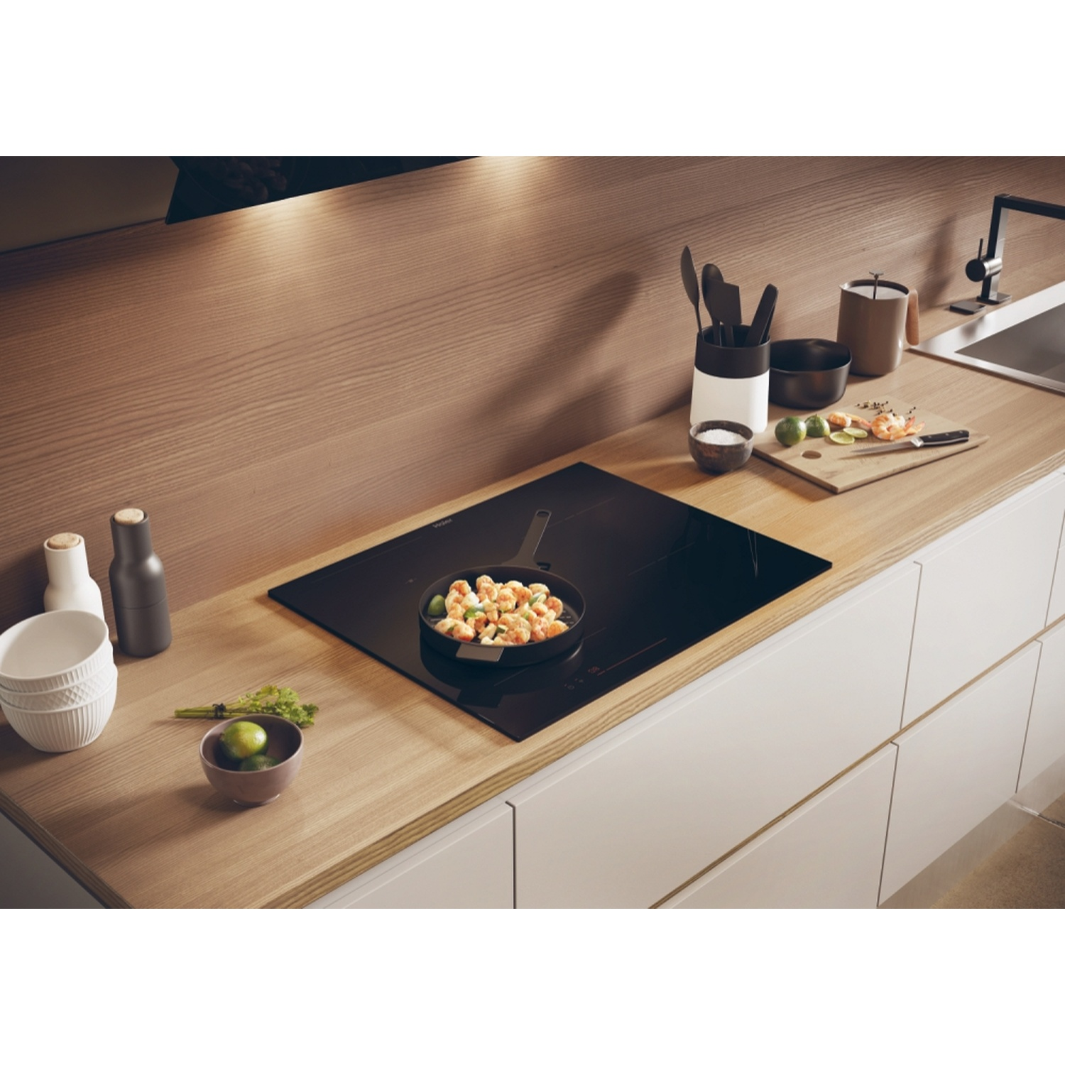 Un piano cottura con padella e ingredienti. Un piano di lavoro in legno.