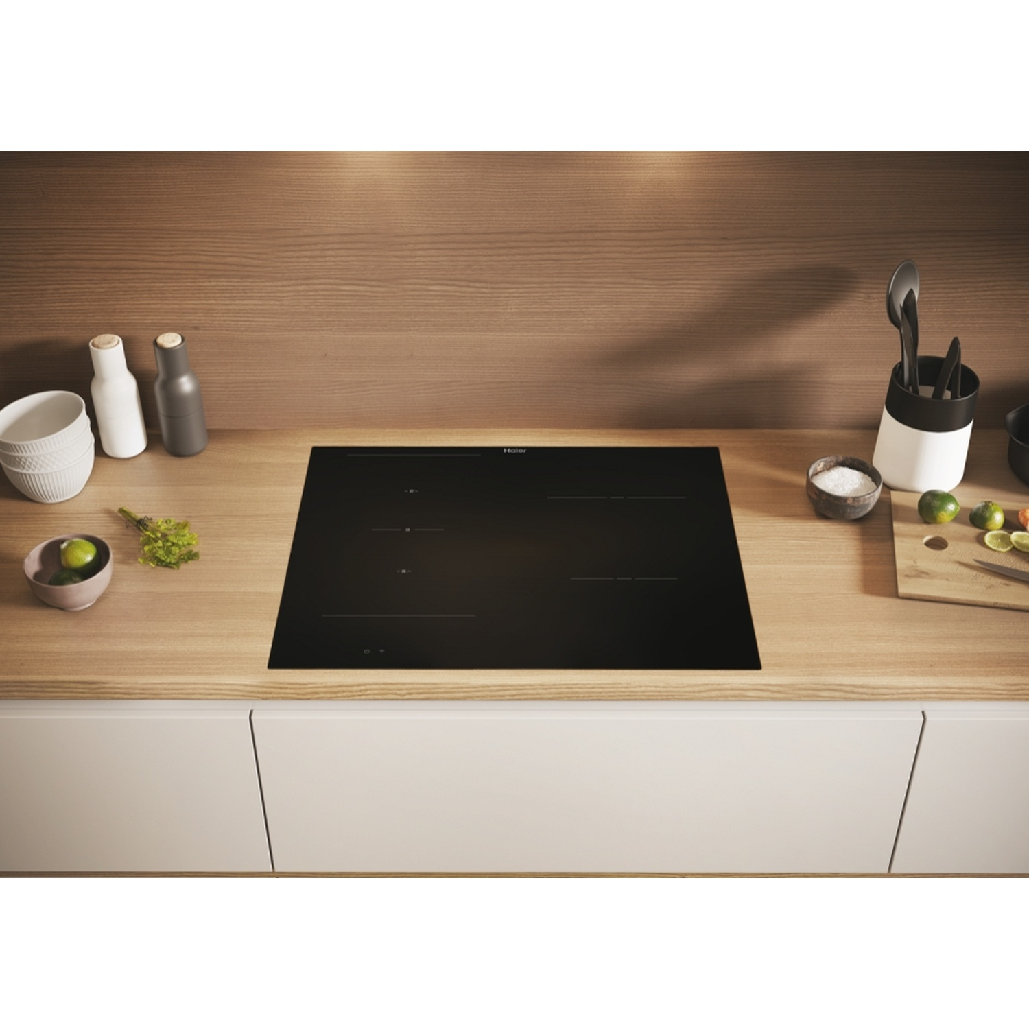 Un piano cottura a induzione nero su un piano di lavoro in legno con utensili e frutta.