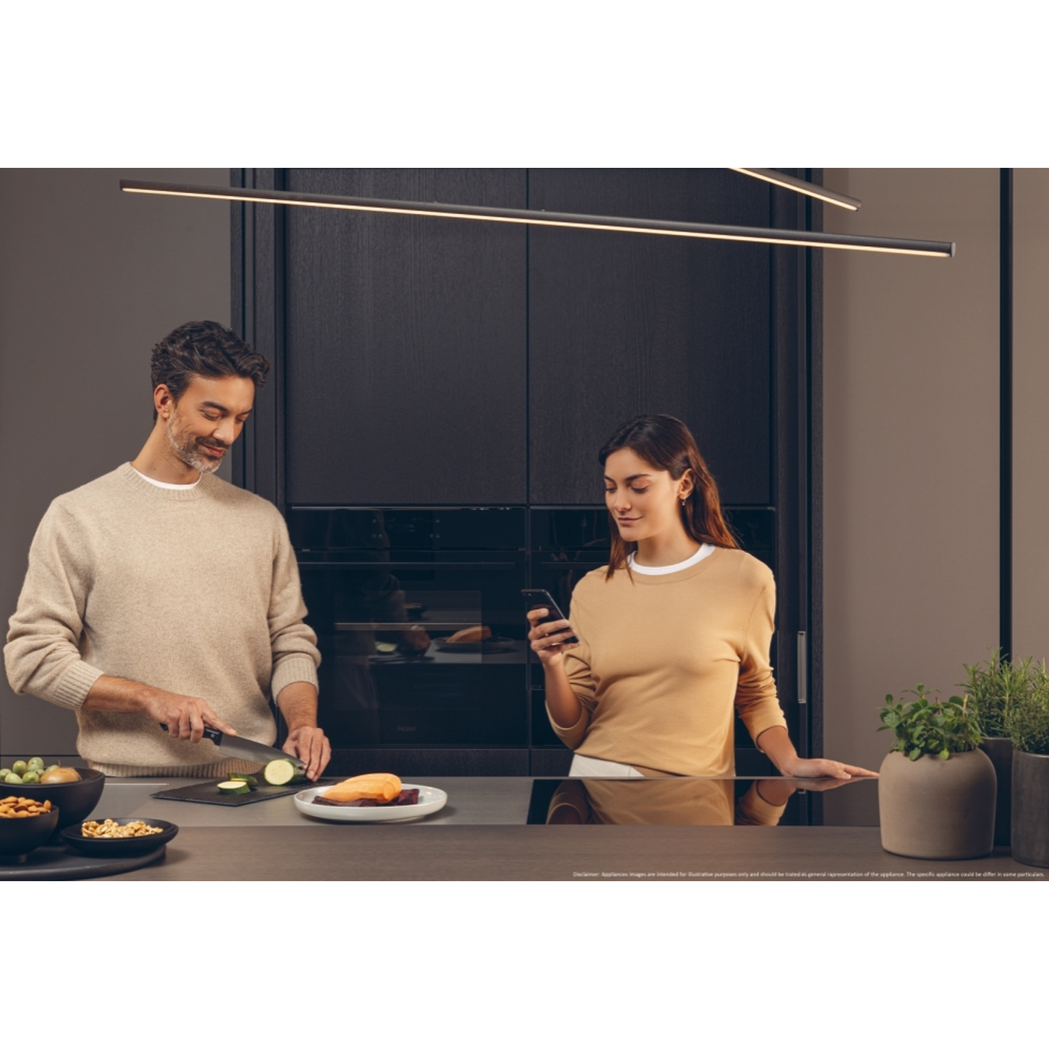 Uomo taglia zucchine, donna guarda il telefono in cucina moderna.