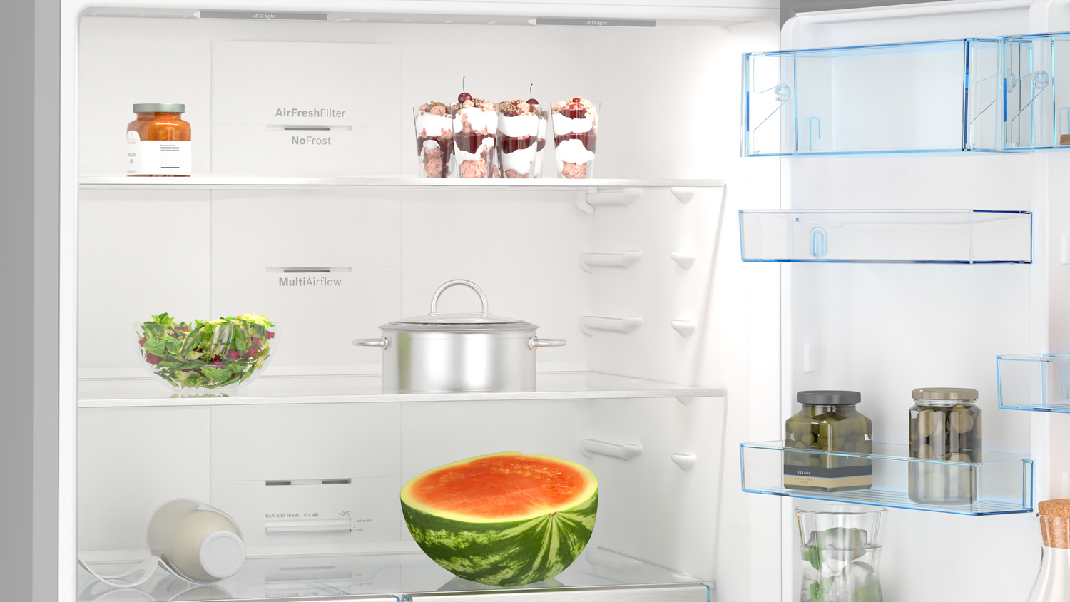 Un refrigerador abierto con vasos de postres, ensalada, olla, sandía y tarros.