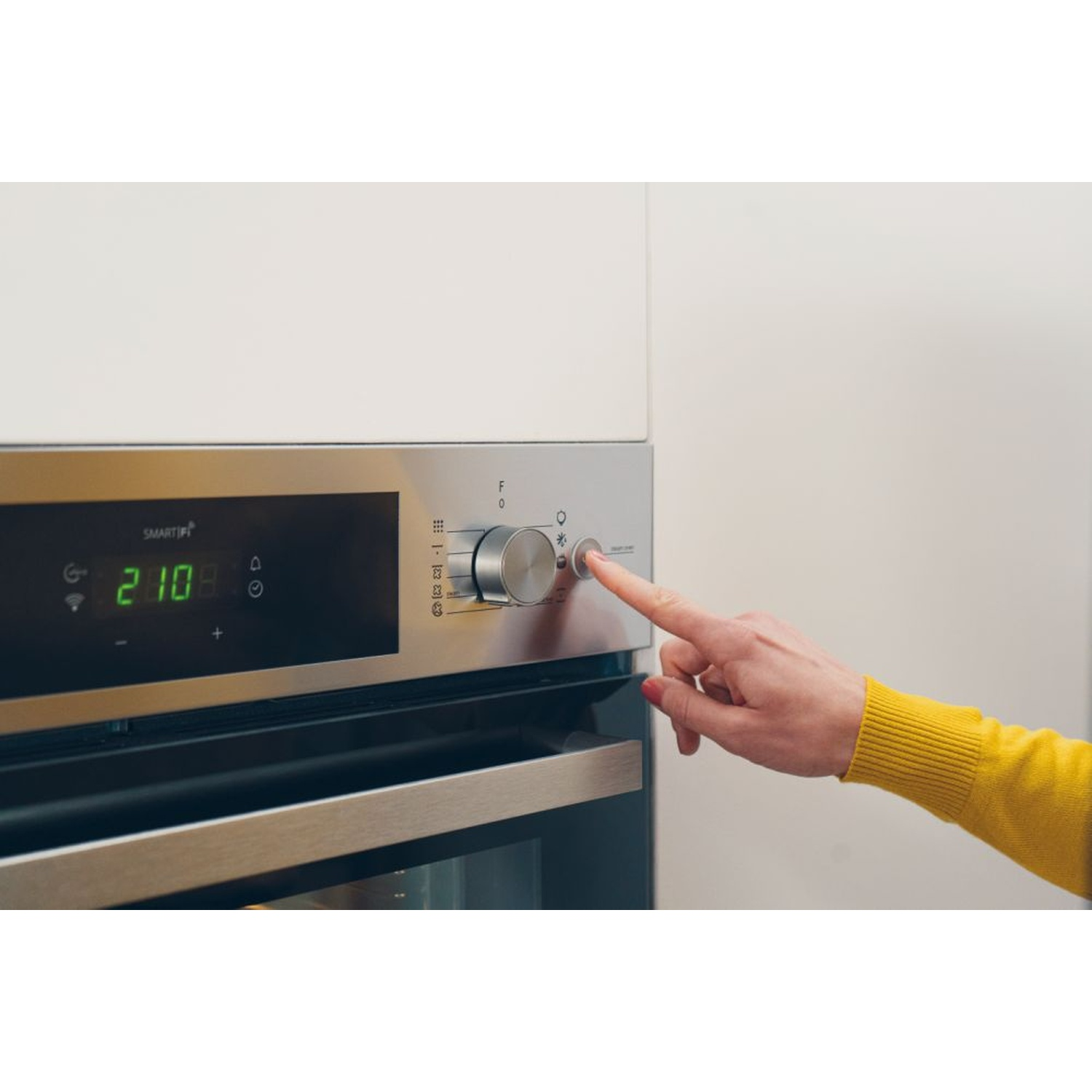 Una mano preme un pulsante su un forno moderno con display digitale.