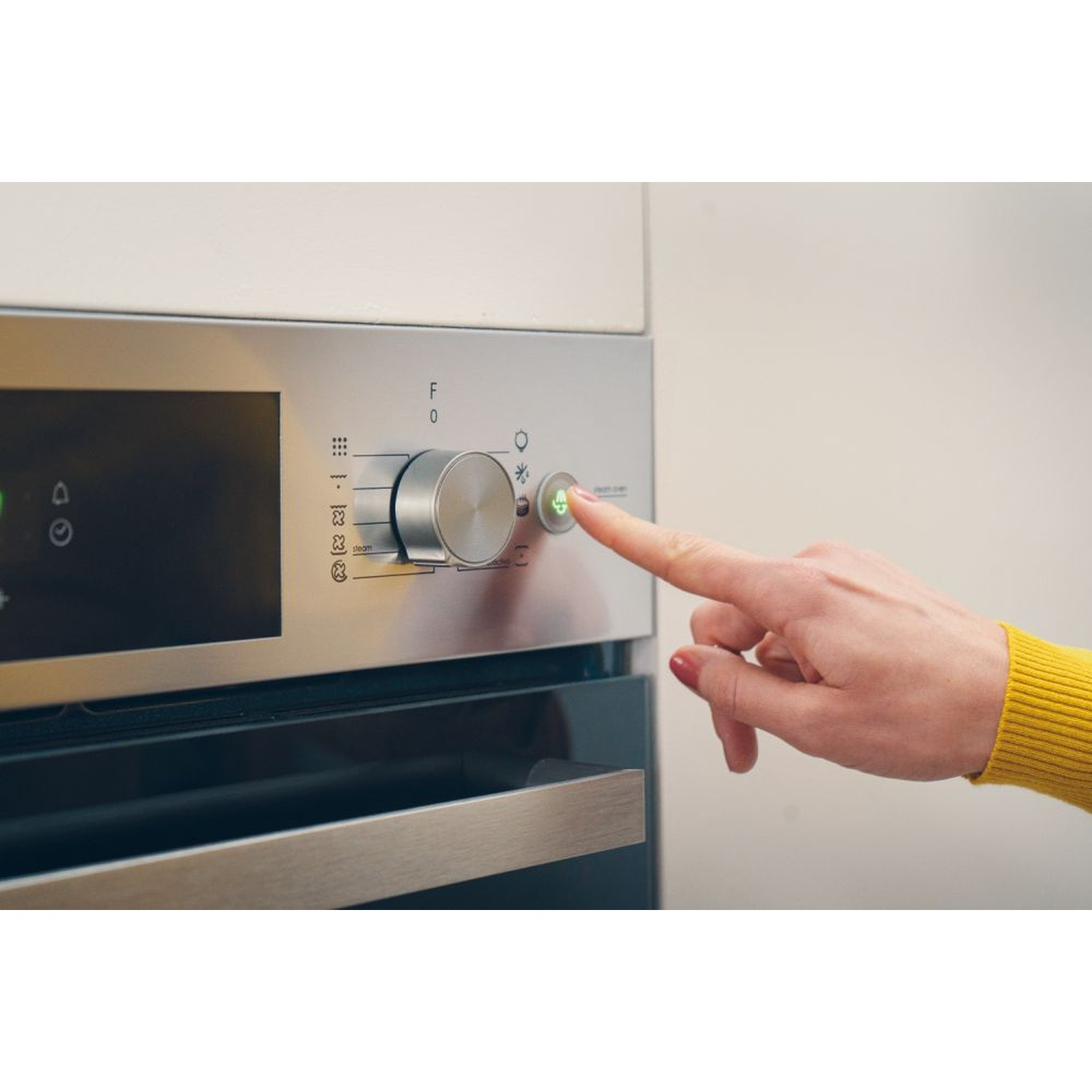Una mano preme un pulsante su un forno con luce verde.