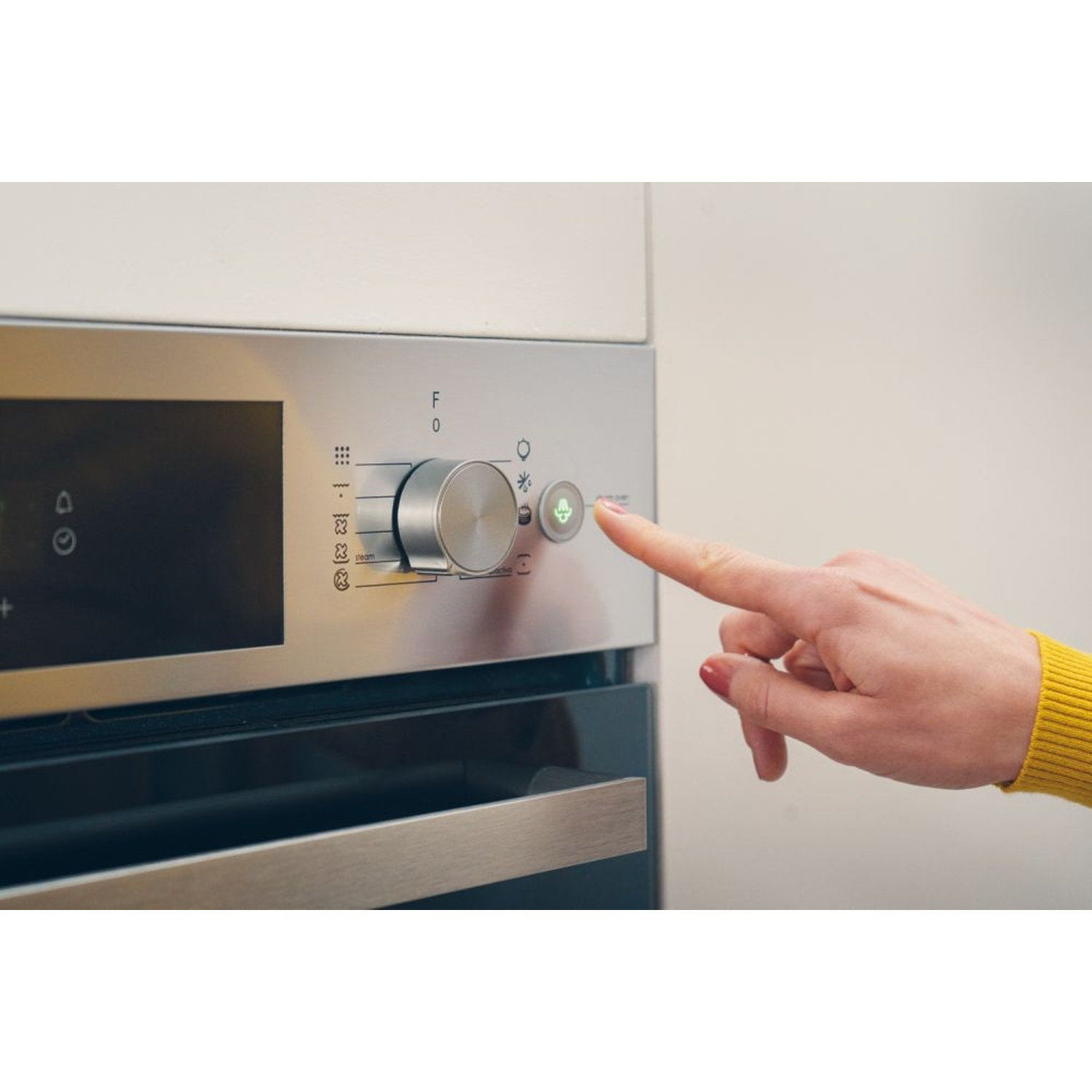 Una mano preme un pulsante verde sul pannello di controllo di un forno.