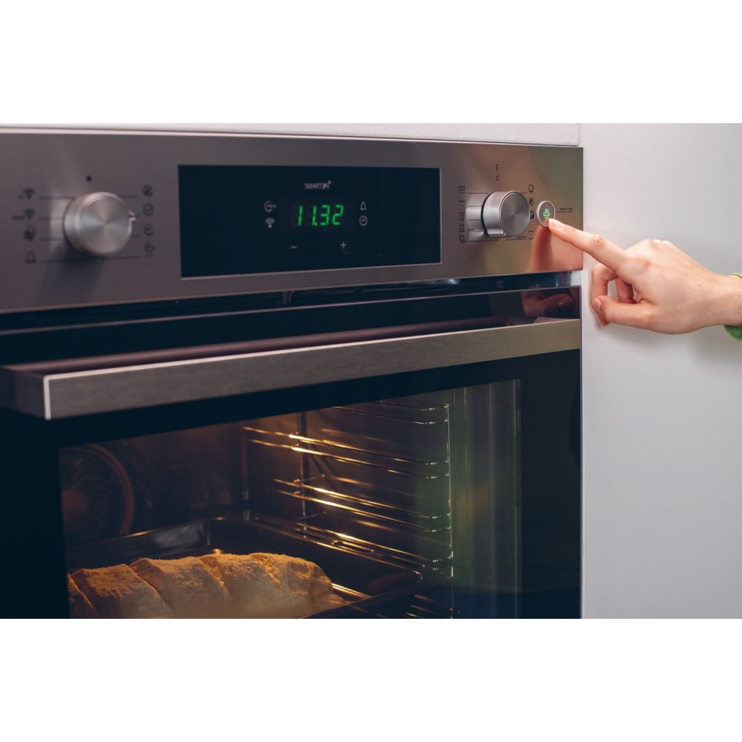 Un dito preme il pulsante di accensione di un forno moderno con display illuminato.