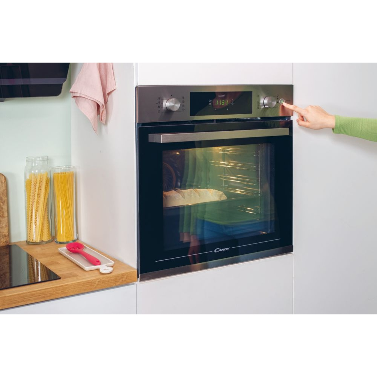 Una mano preme un pulsante su un forno. Dentro cuoce il pane.