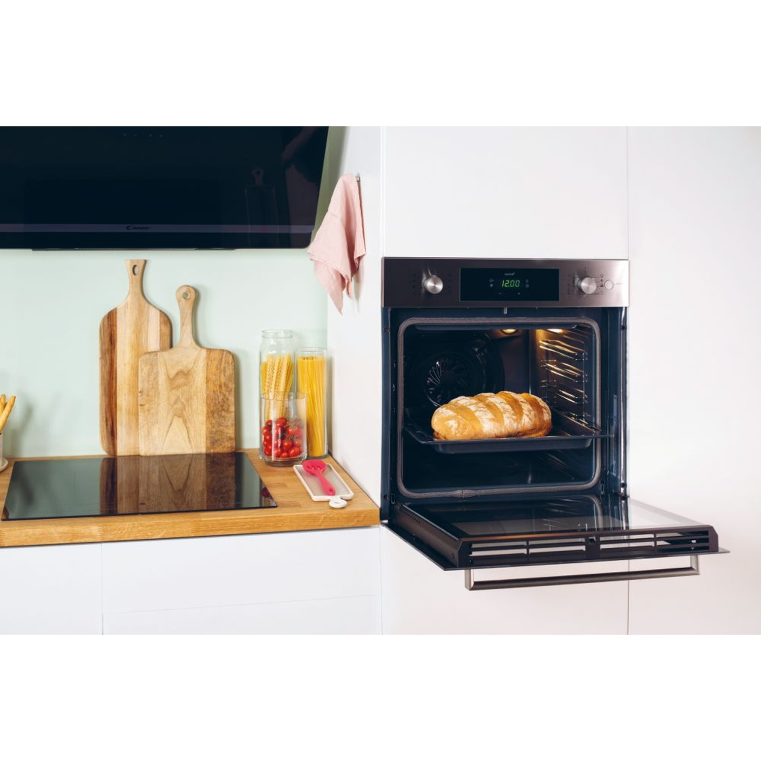 Una pagnotta cuoce in un forno aperto. Taglieri e pasta sono nelle vicinanze.