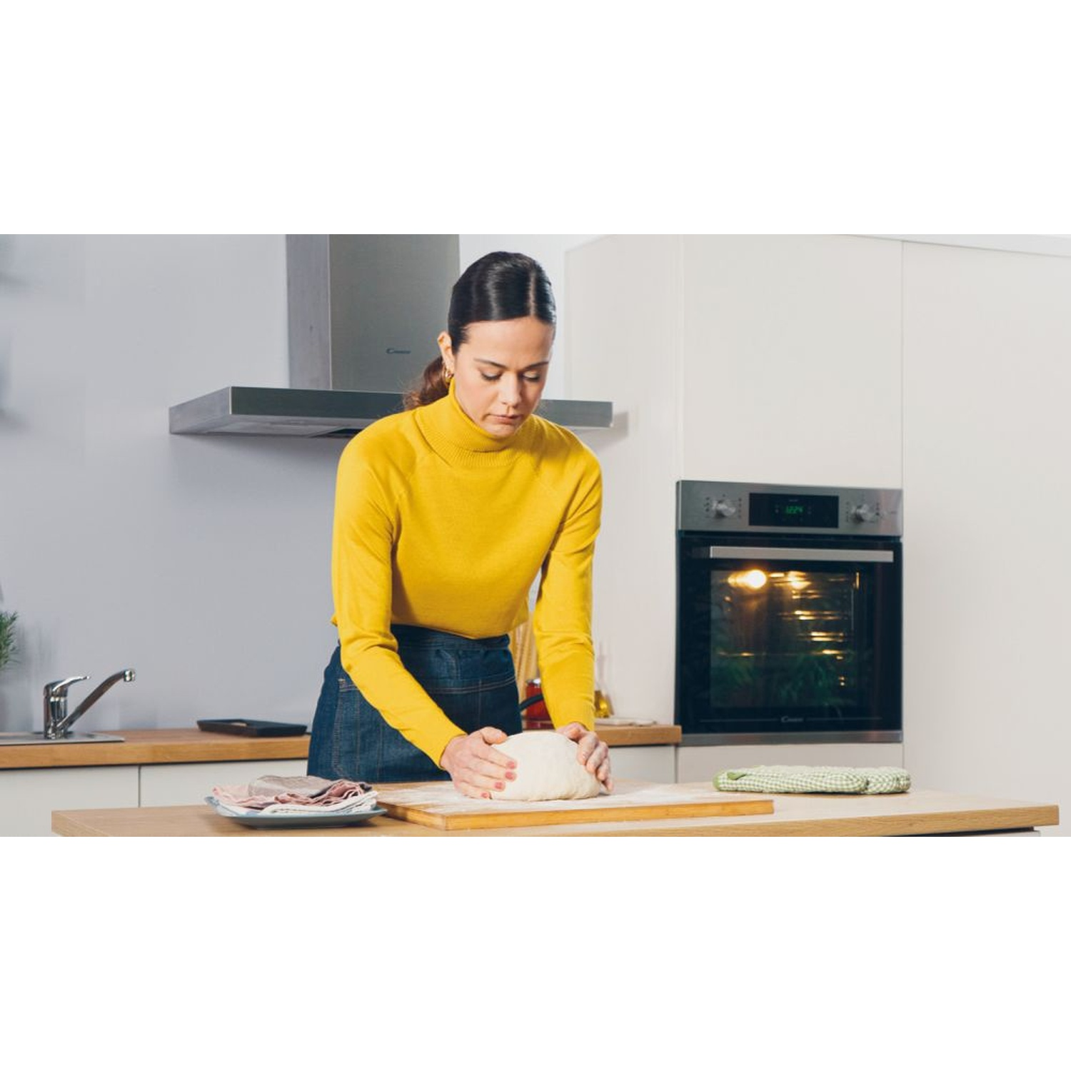 Una donna con maglione giallo impasta in una cucina moderna.