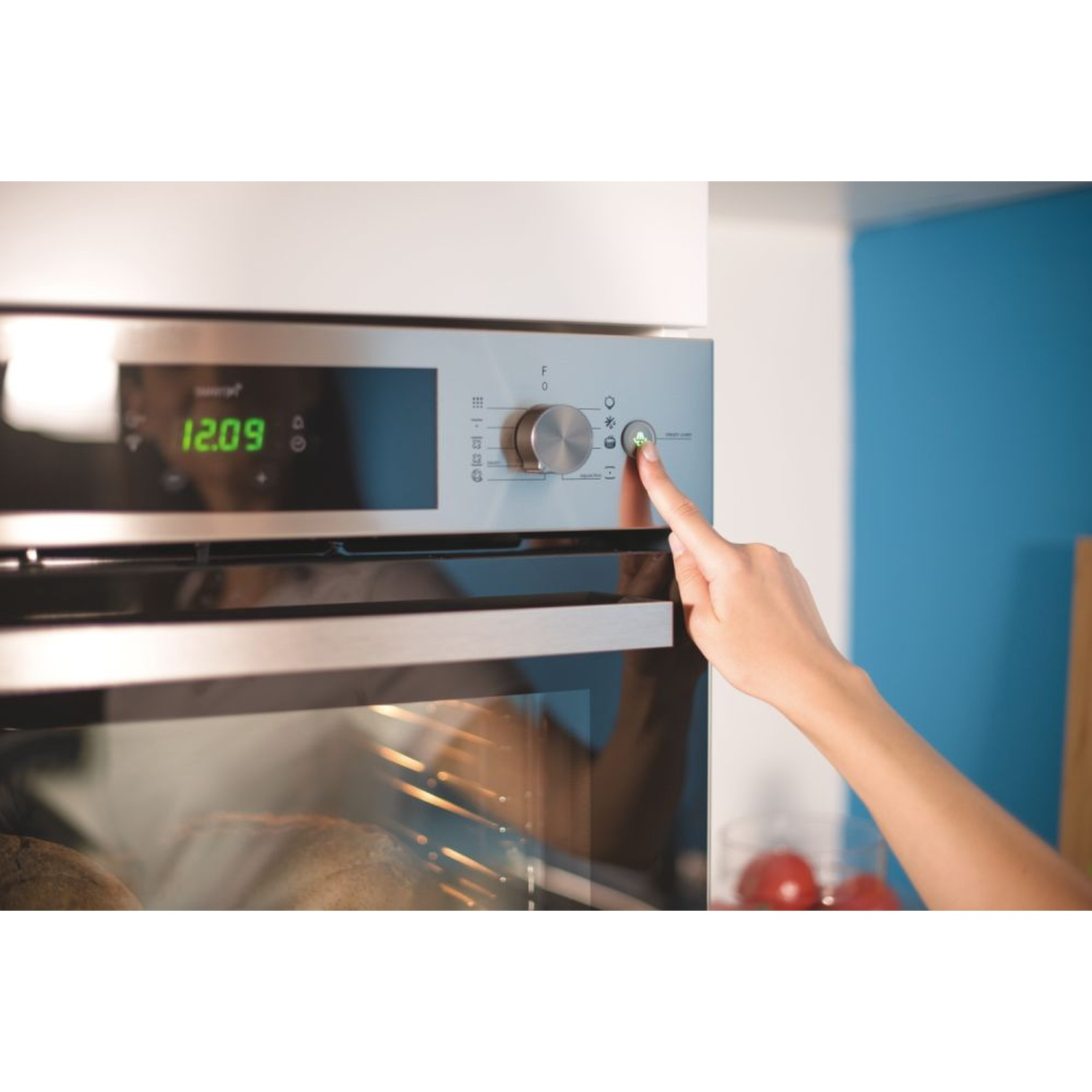 Una mano preme un pulsante su un forno con display digitale.