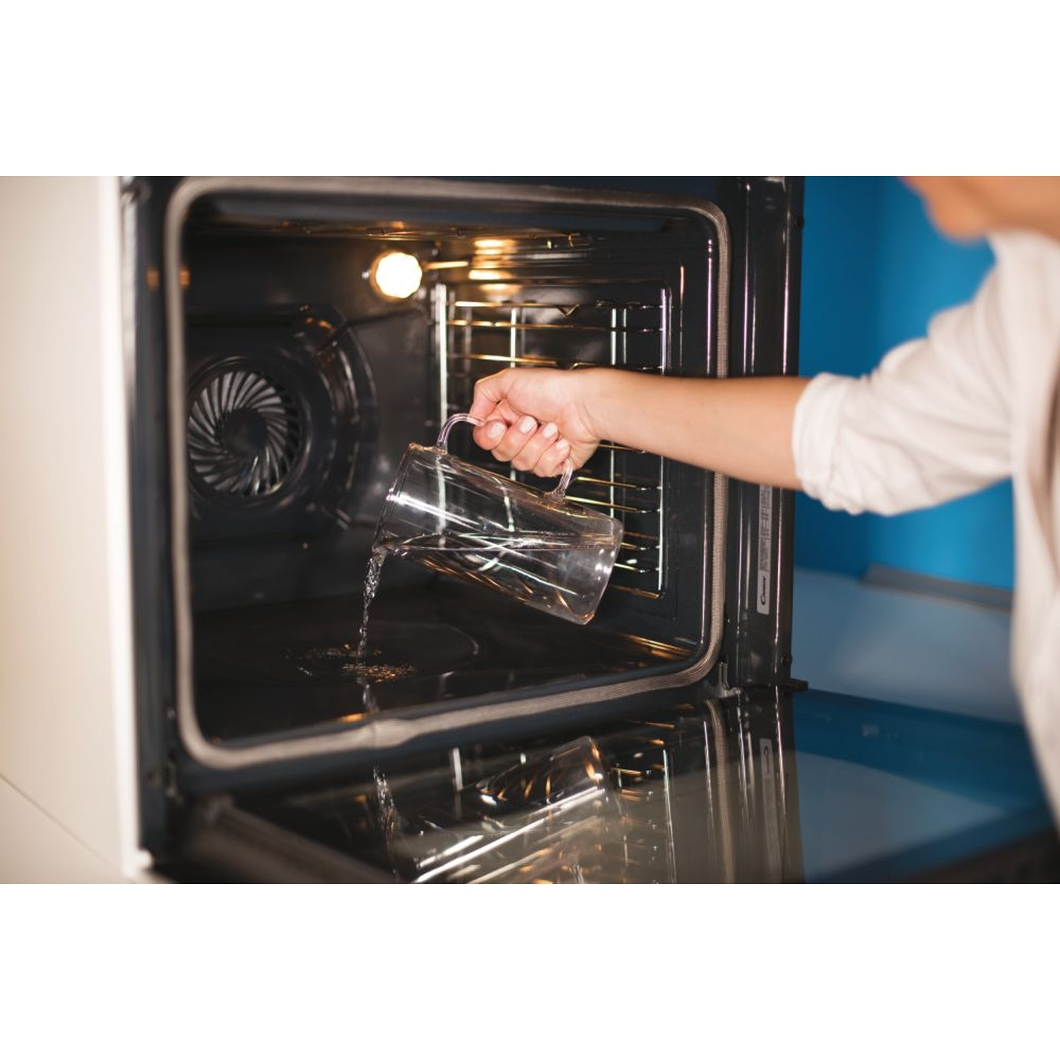 Una persona versa acqua da una brocca di vetro in un forno aperto.