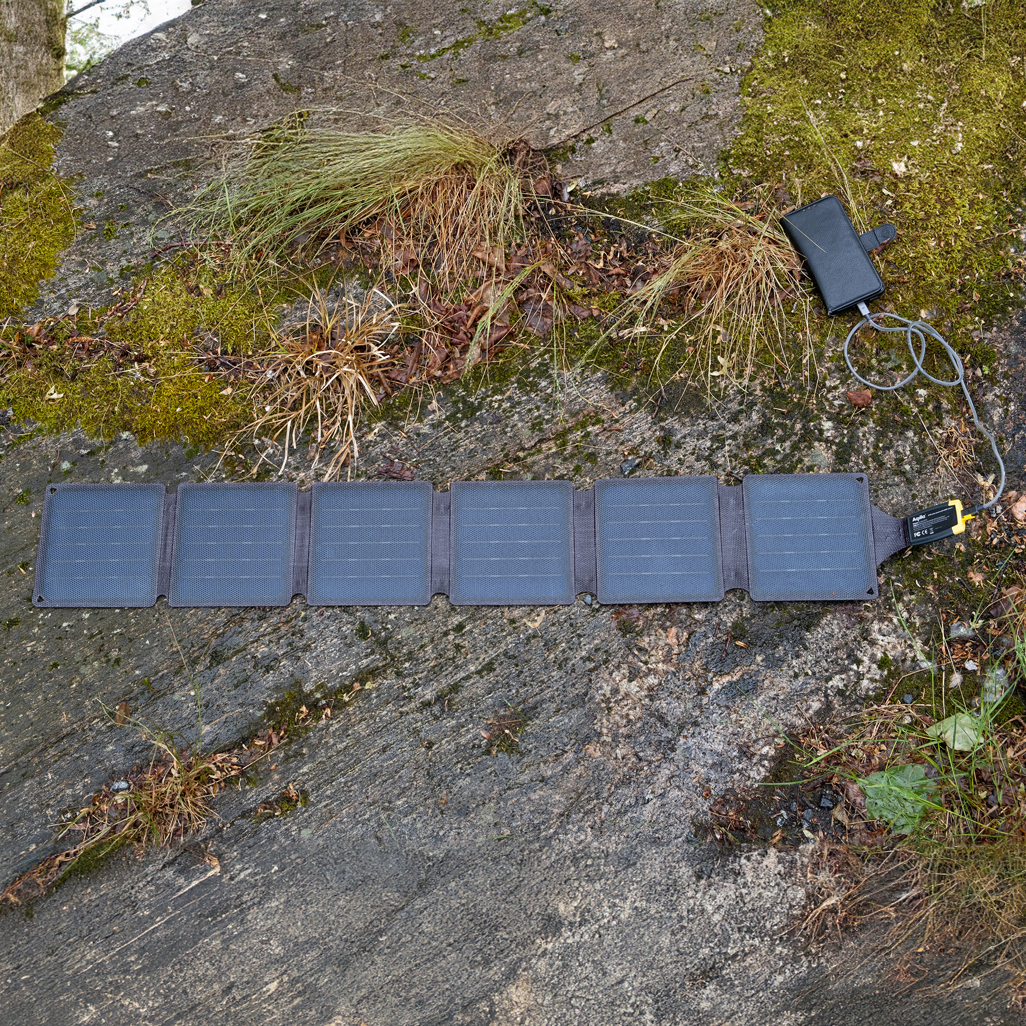 Ein faltbares Solarpanel ist auf einem Stein mit Moos und Gras ausgelegt.