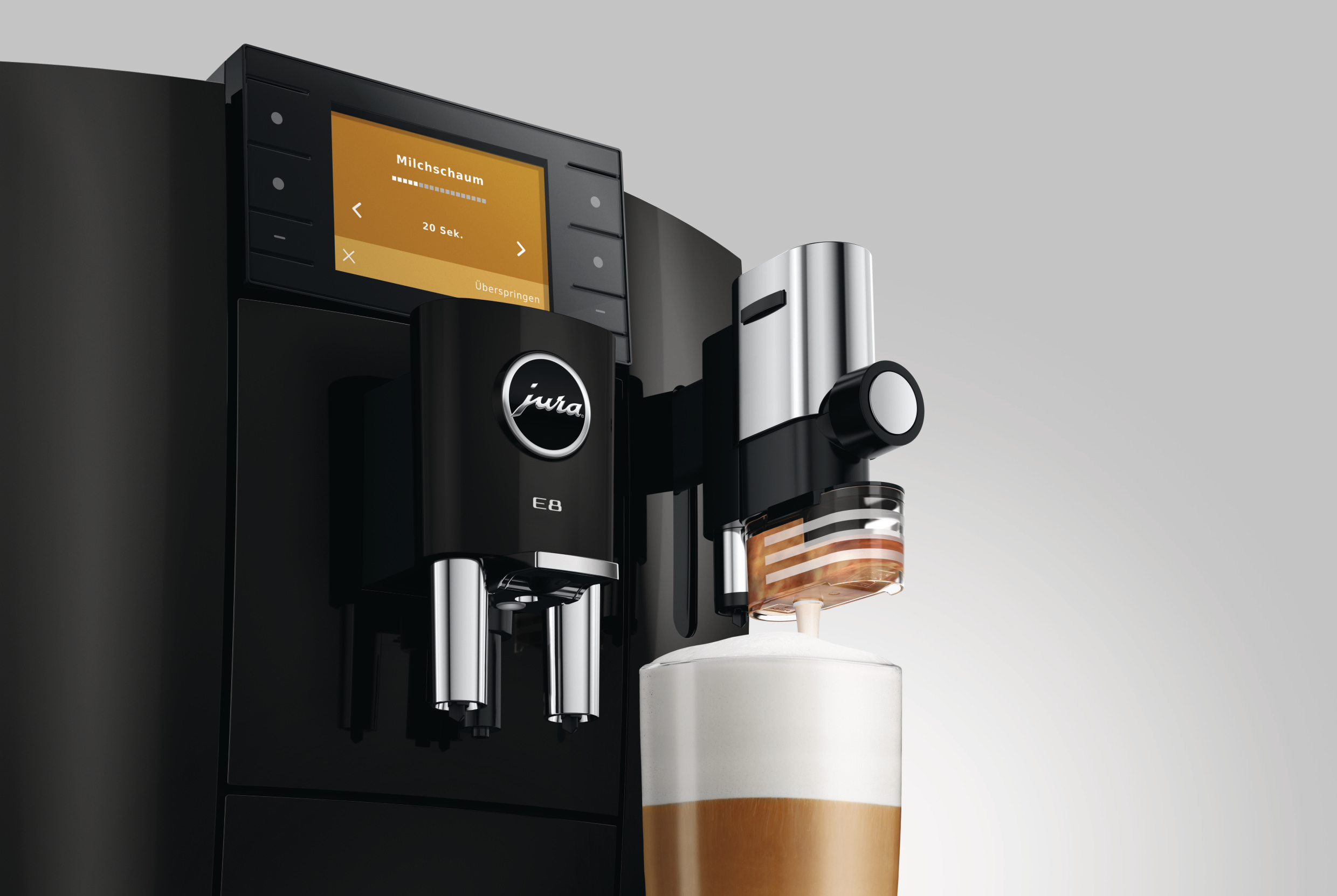 Schwarze Kaffeemaschine mit Milchschaum, der in ein Glas fließt.