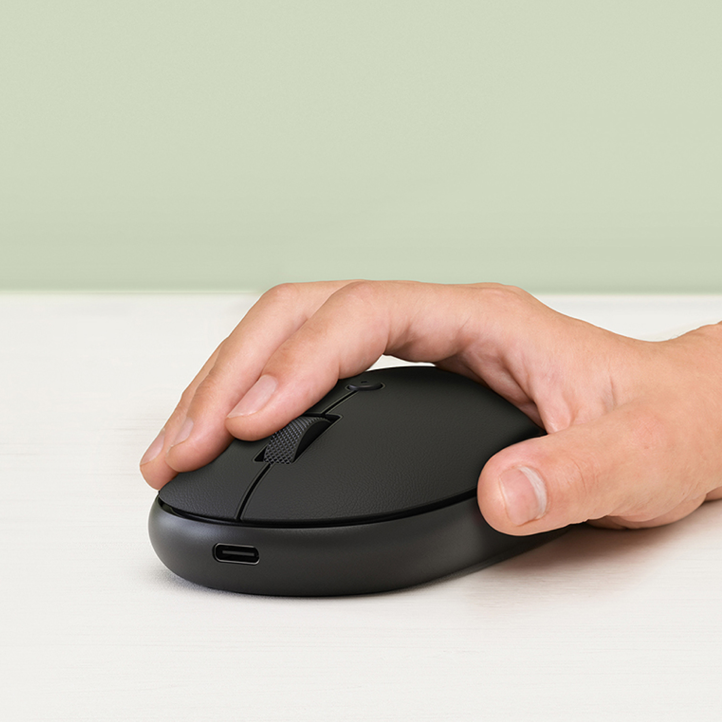 Una mano usa un mouse nero su una scrivania chiara.
