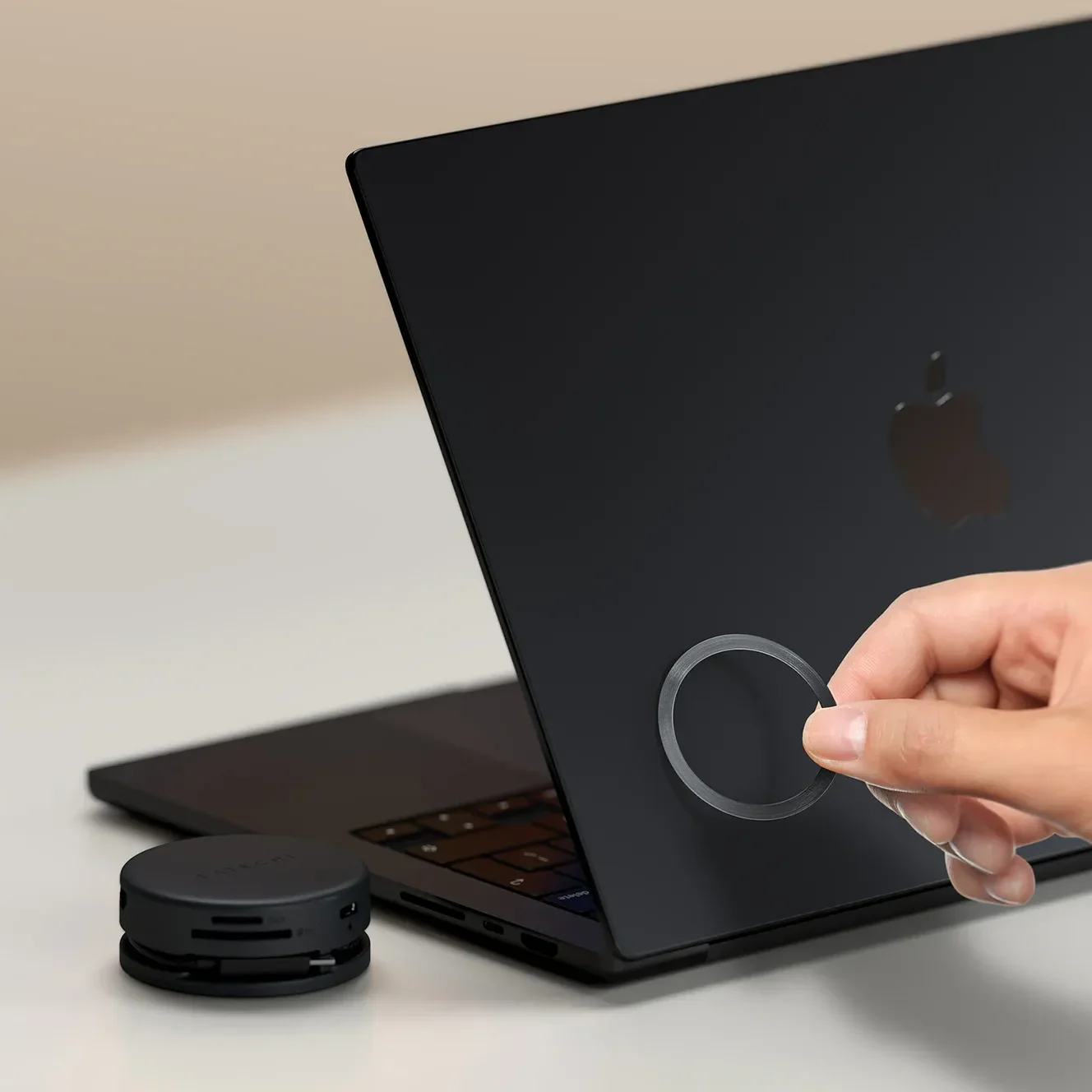 Mano posiziona anello su laptop nero. Piccolo cerchio nero accanto.