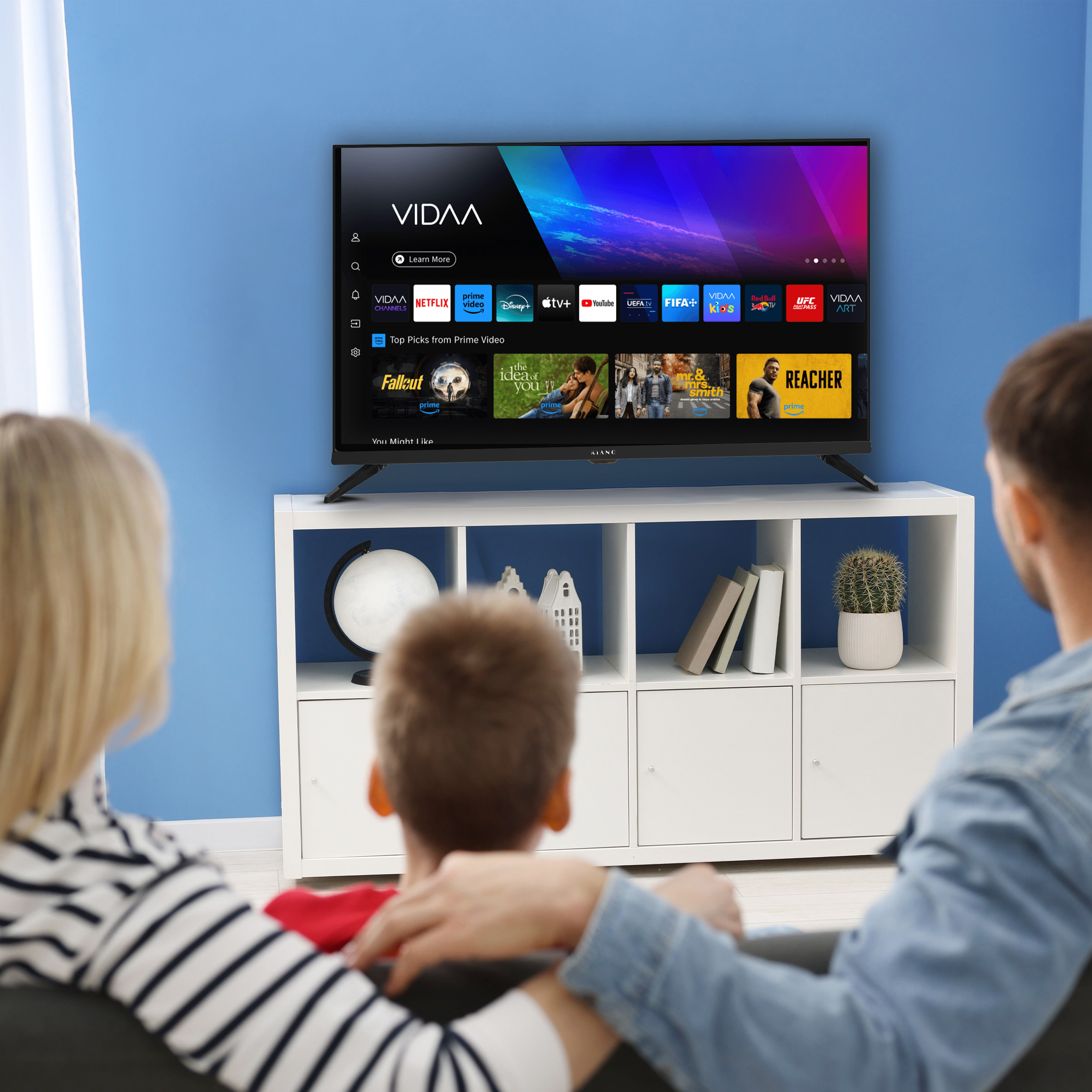 Rodzina ogląda TV z aplikacjami jak Netflix i Prime Video. Półki z dekoracjami.