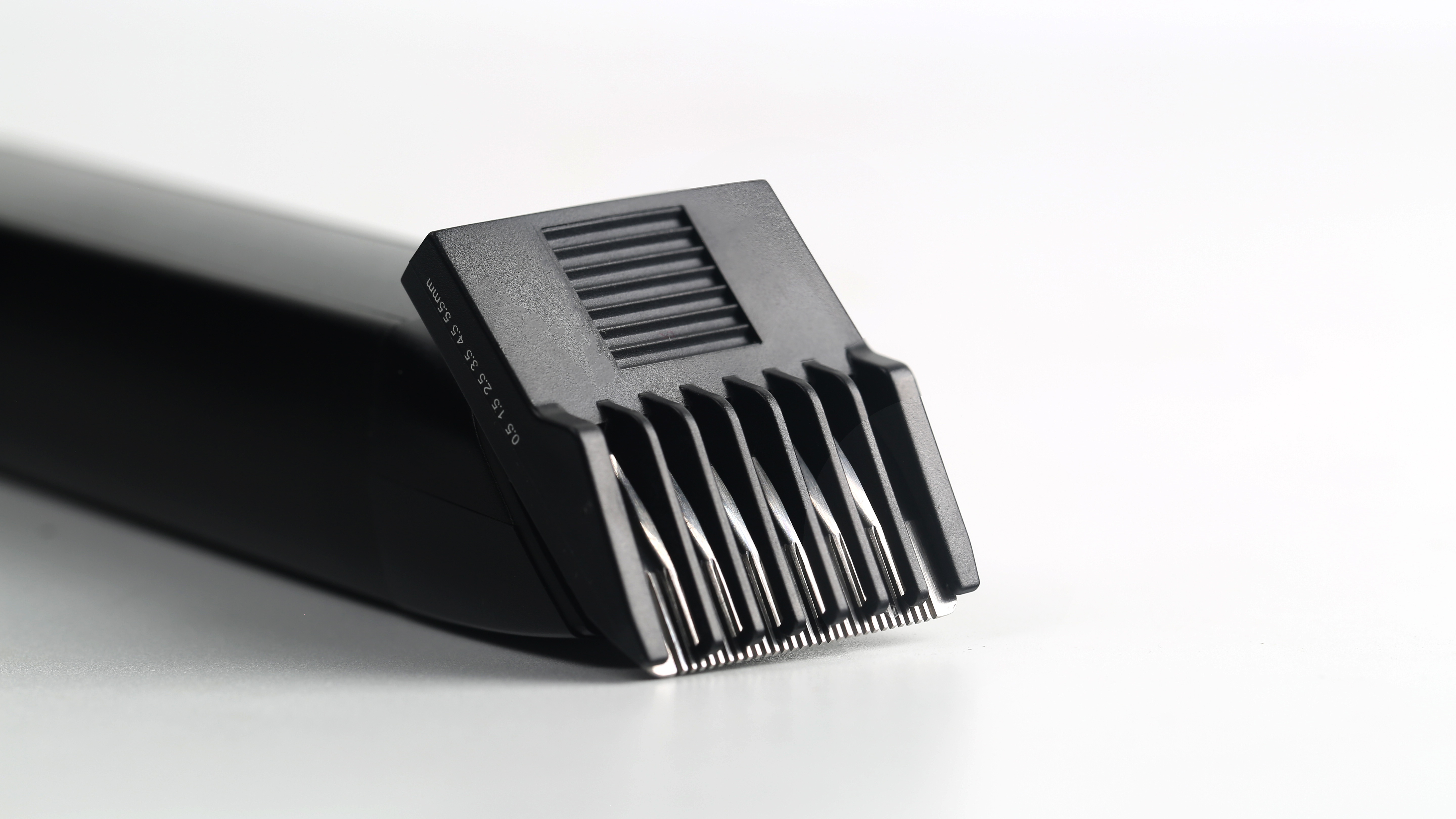 Zbliżenie czarnej maszynki z metalowymi ostrzami i oznaczeniami długości.