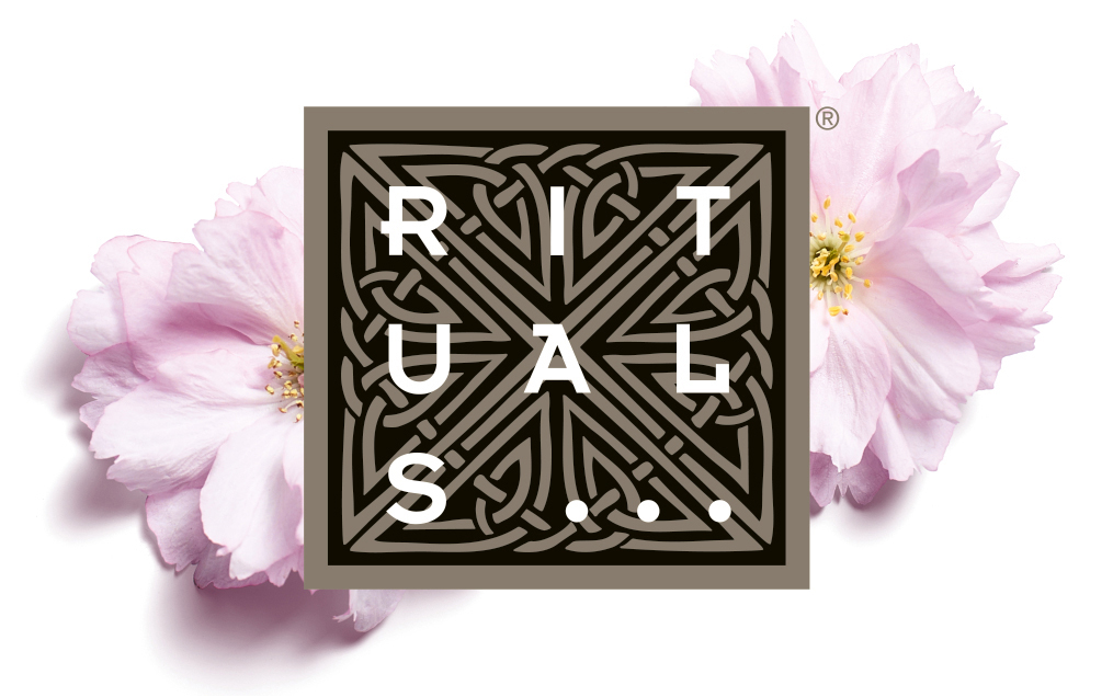 Rituals-Logo mit zweifarbigem Muster, flankiert von rosa Kirschblüten.