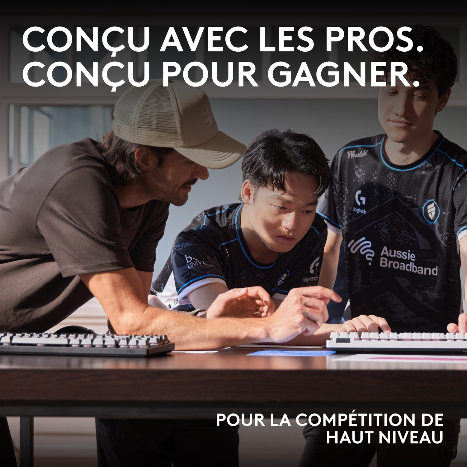 Trois hommes en maillots e-sport regardent des claviers. Texte dessus et dessous.