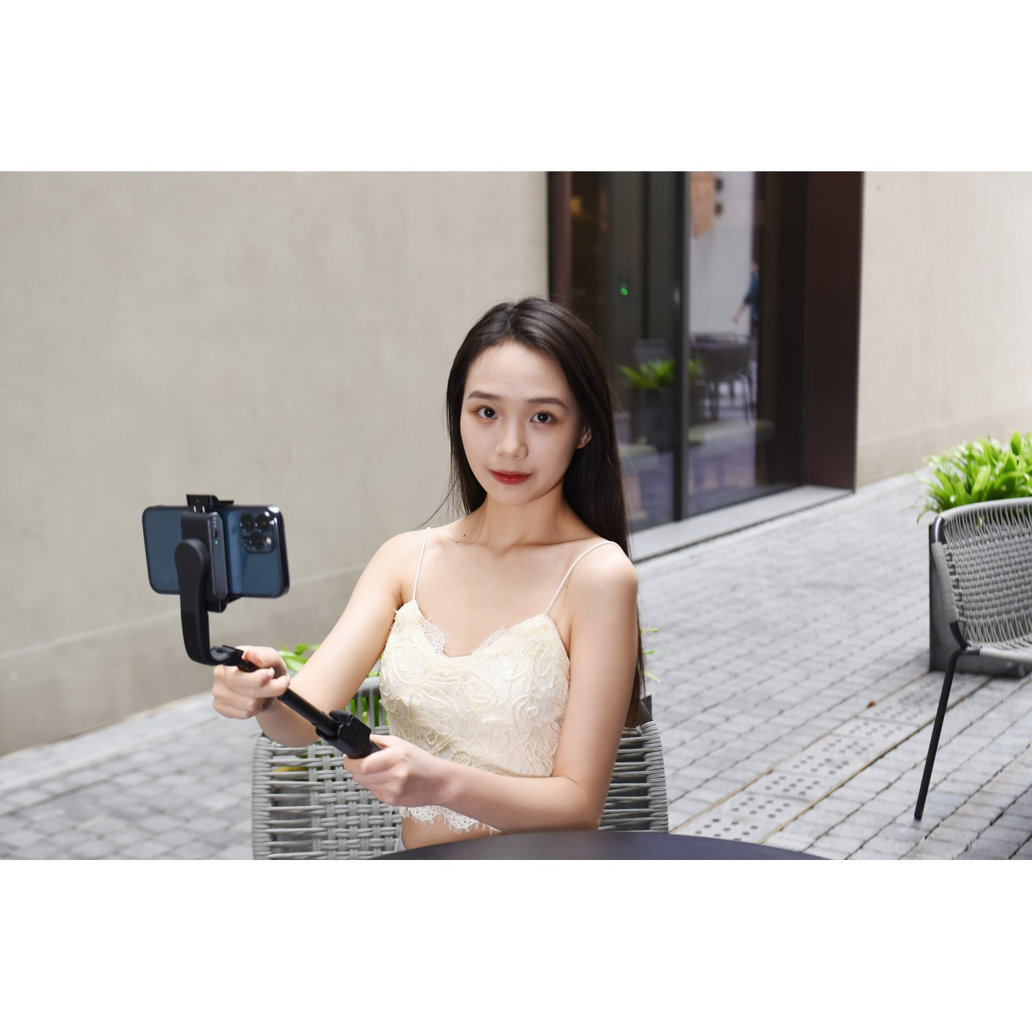 Donna con gimbal e telefono seduta a un tavolo all'aperto.