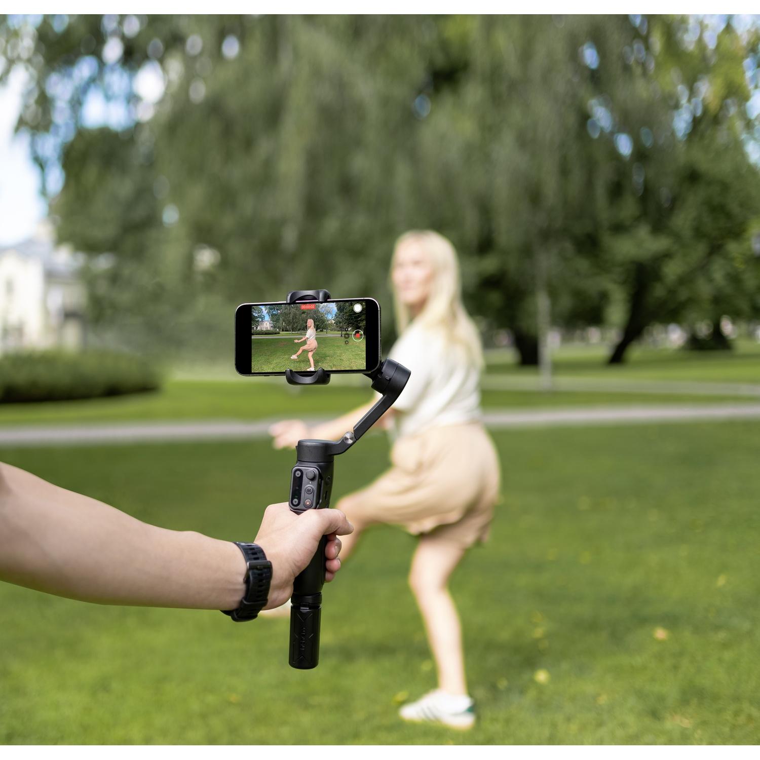 Un gimbal tiene un telefono che riprende una donna che balla in un parco.