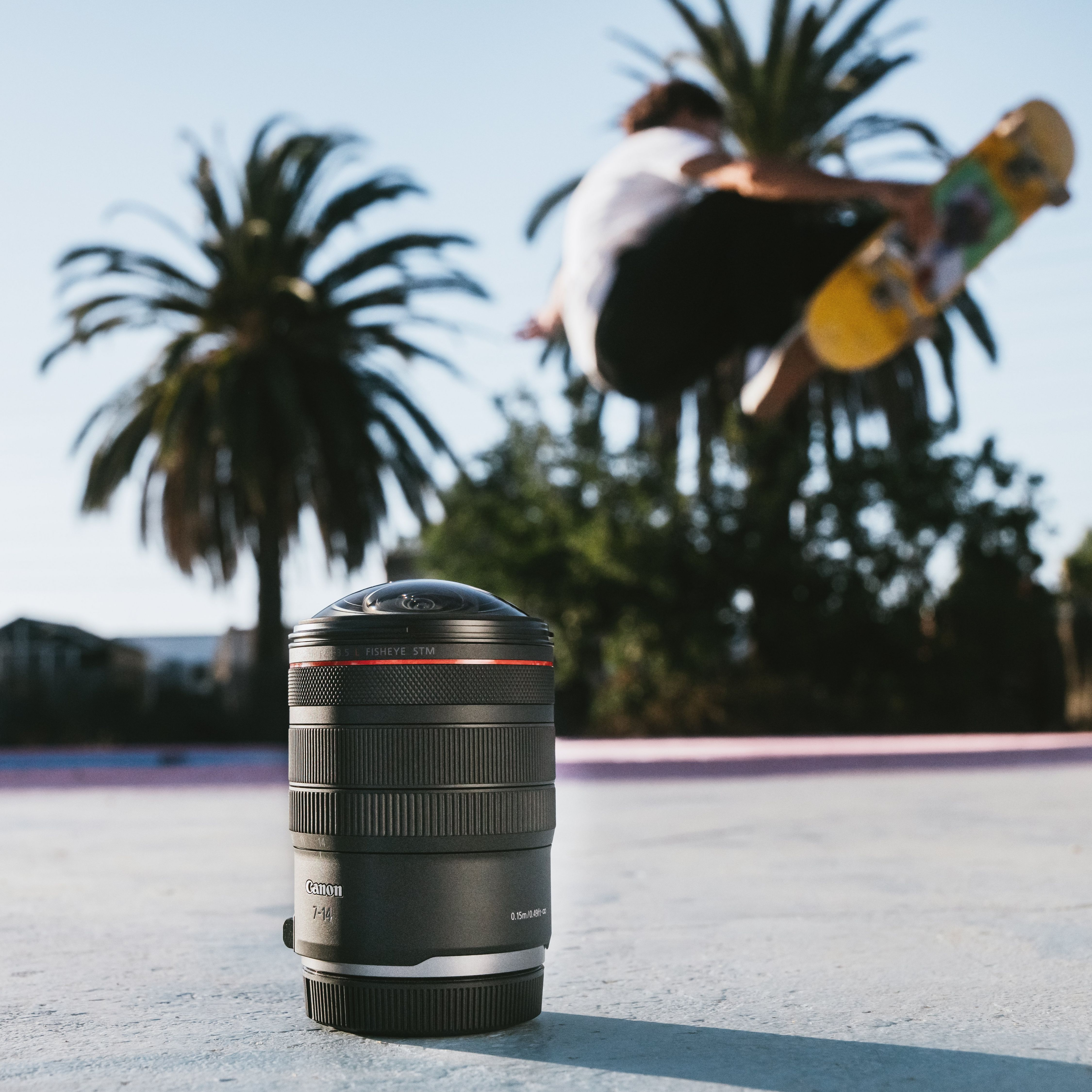Un objectif fisheye au premier plan, un skateur saute en arrière-plan.